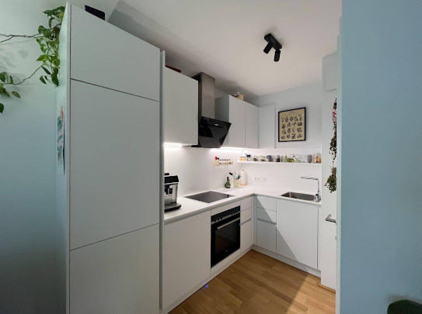 Moderne weiße Einbauküche mit integrierten Geräten und Holzfußboden.