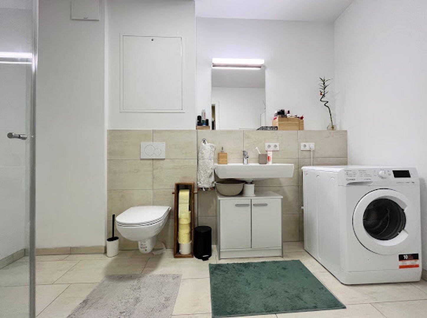 Funktionales Badezimmer mit Dusche, WC, Waschbecken und Platz für eine Waschmaschine.