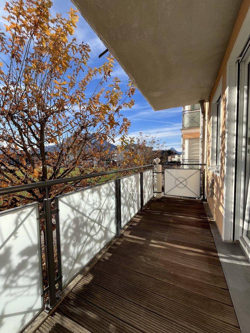 Langer Balkon mit Holzboden und Metallgeländer, umgeben von Herbstbäumen mit Bergblick.