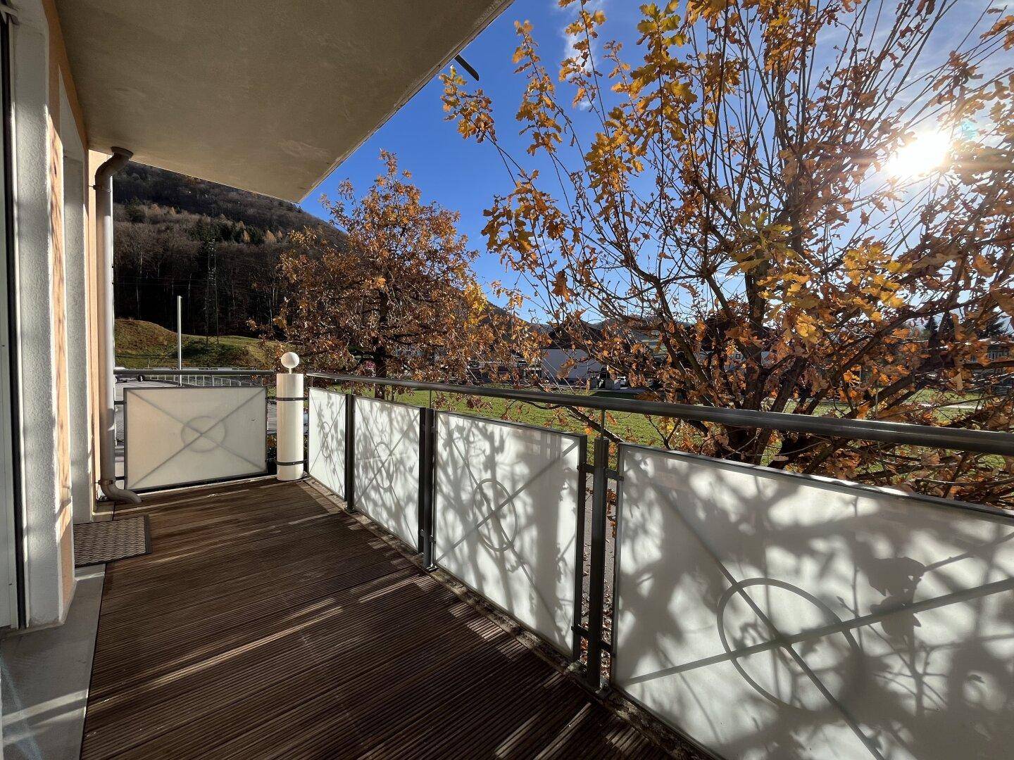 Sonniger Balkon mit Holzboden und Blick auf die umliegende Berglandschaft und Bäume.