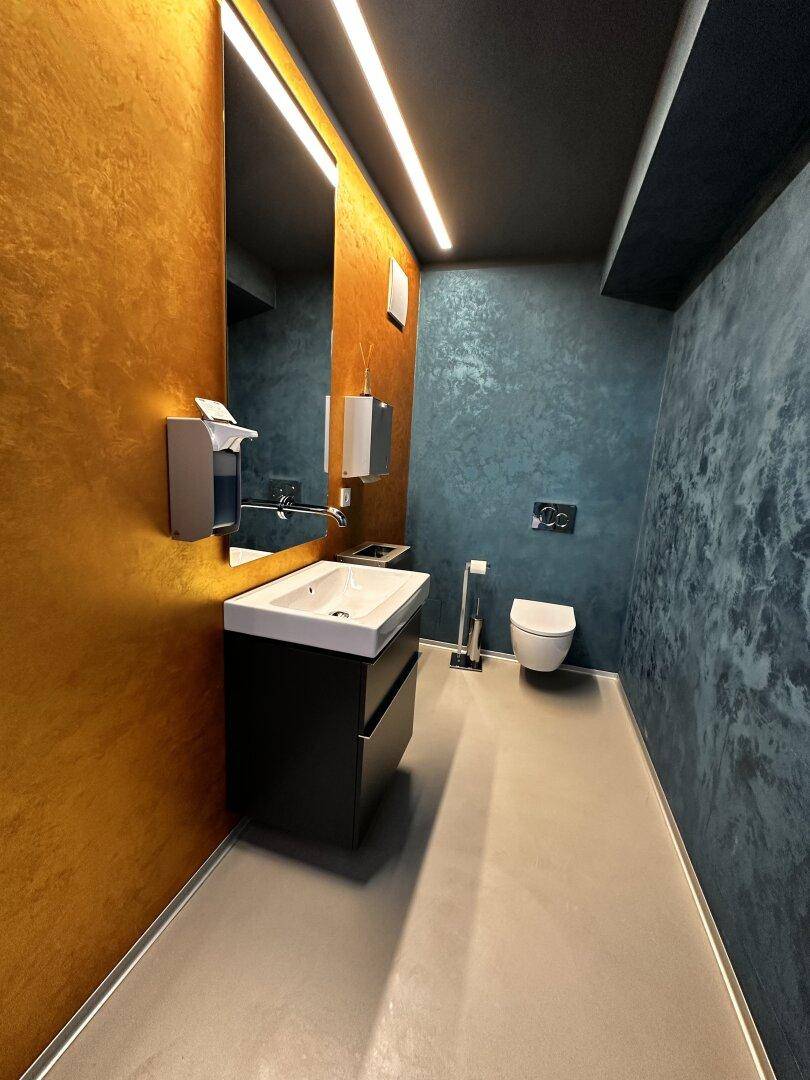 Stilvolle Toilette mit goldener und blauer Akzentwand, modernem Waschbecken und Wand-WC.
