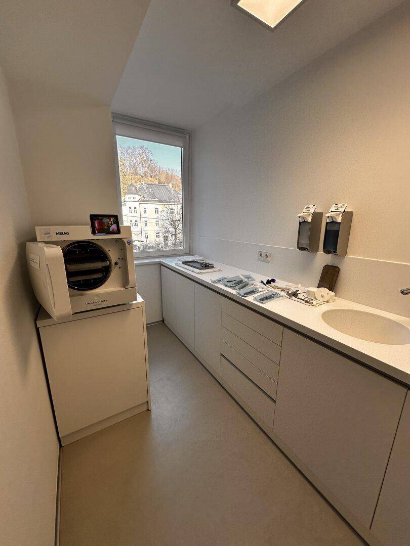 Funktionaler Sterilisationsraum mit Arbeitsplatte, Spülbecken und Fenster, das Tageslicht hereinlässt.