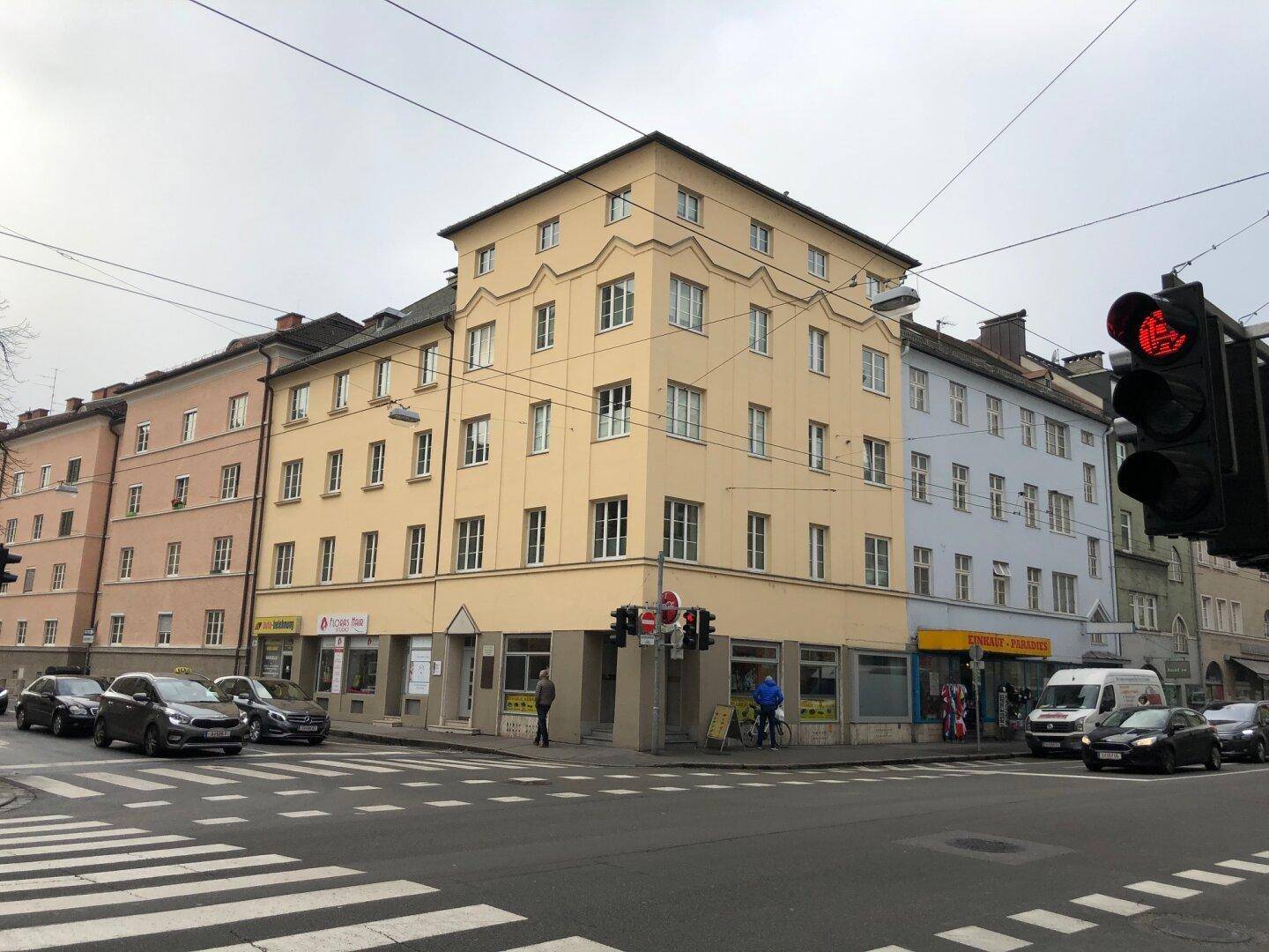 Mehrstöckiges Eckgebäude mit Geschäften im Erdgeschoss und Wohnungen darüber in städtischer Umgebung.