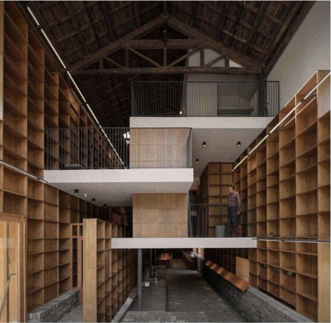 Hoher Innenraum mit mehreren Ebenen, Holzregalen und sichtbaren Dachbalken, ideal für eine Bibliothek.