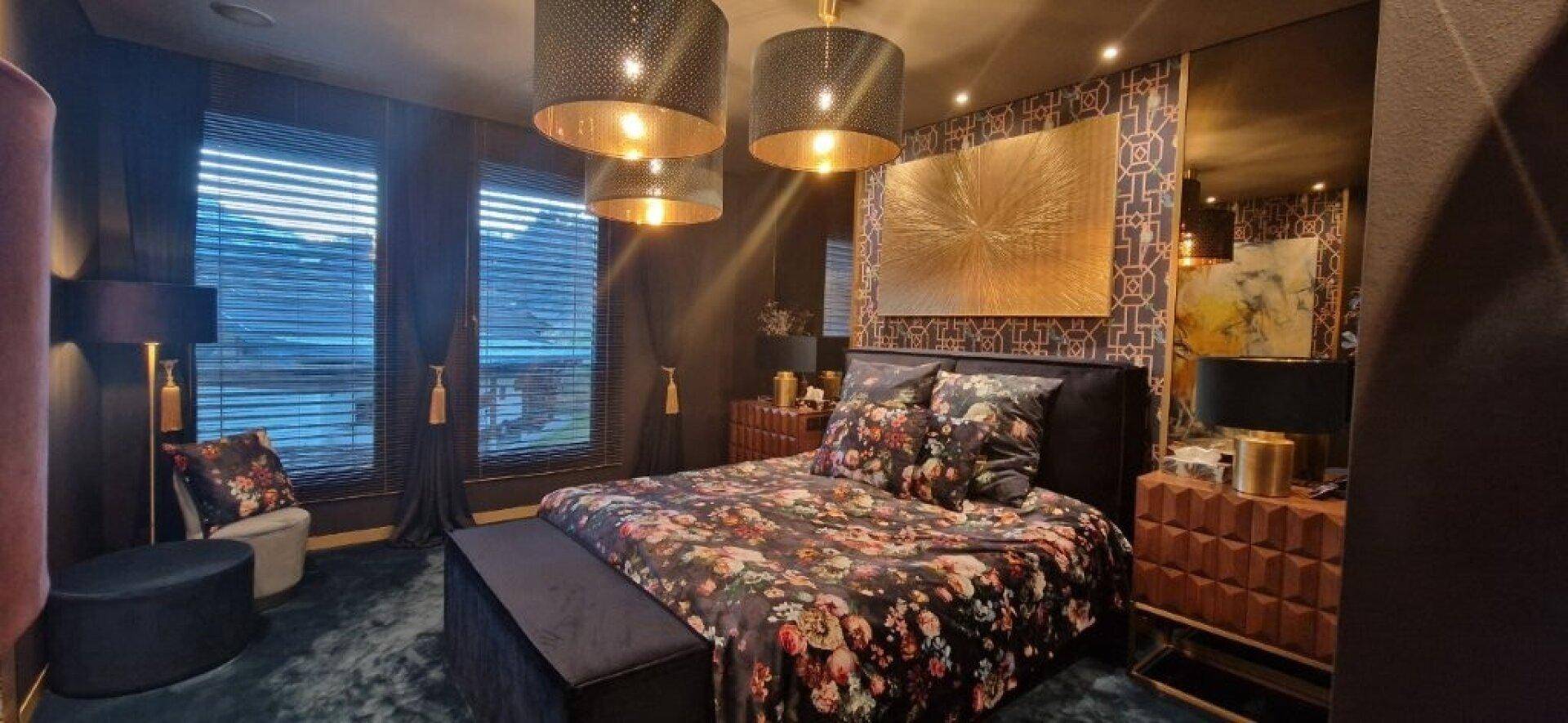 Elegantes Schlafzimmer mit großem Bett, floraler Bettwäsche und großen Fenstern.