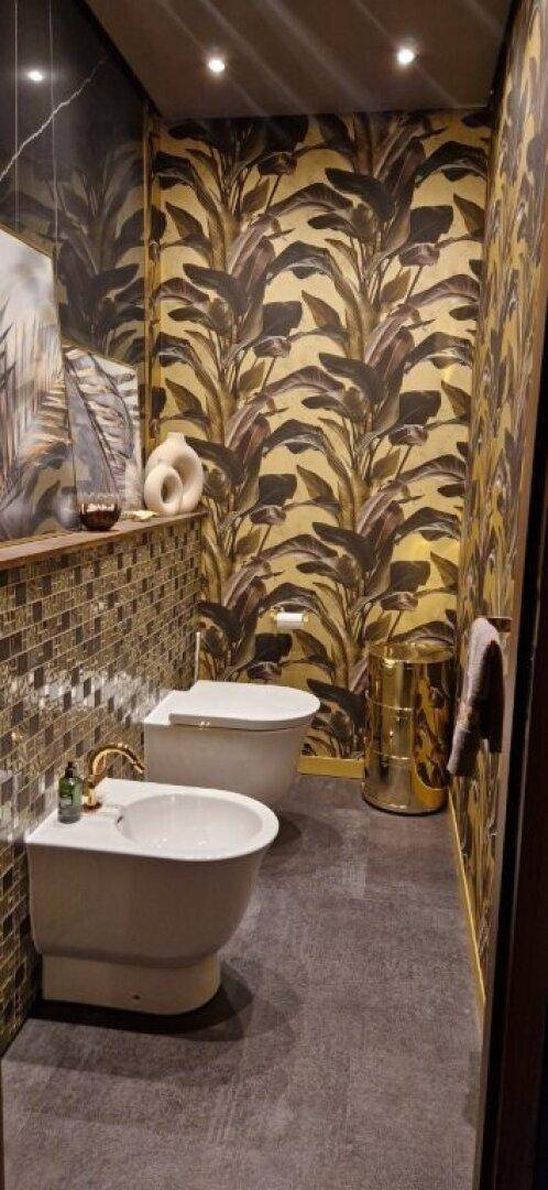 Stilvolles WC mit Bidet und auffälliger Tapete im tropischen Design.