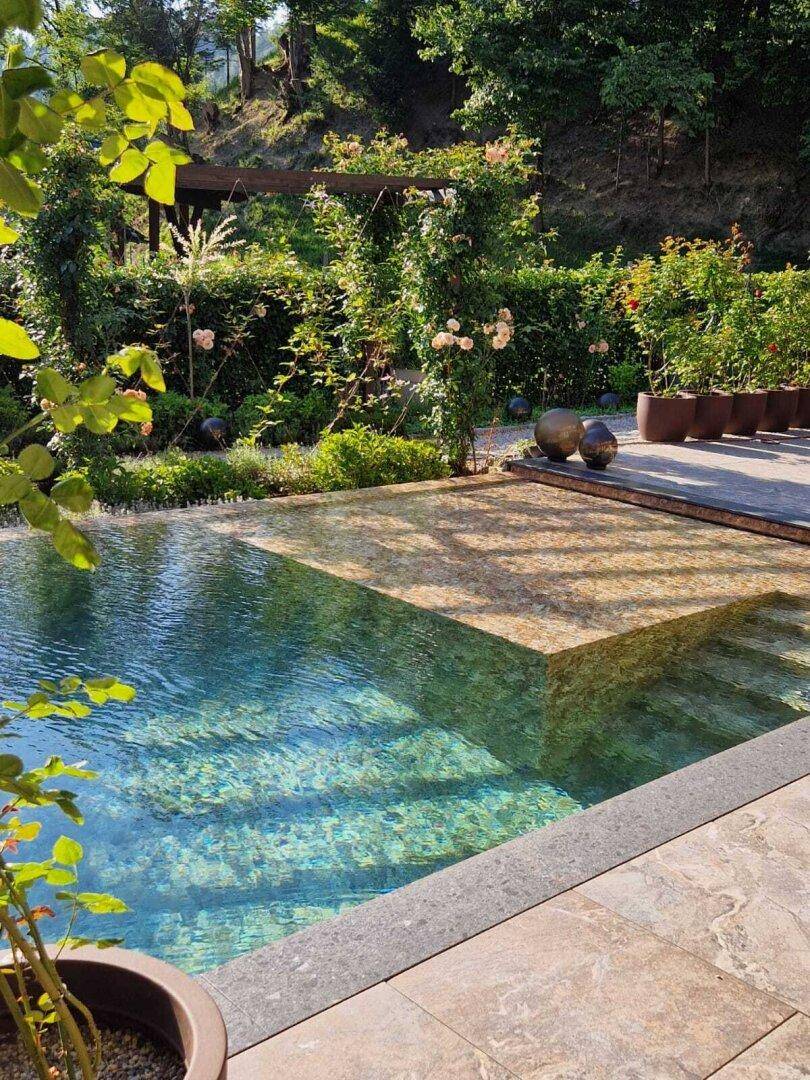 Elegantes Schwimmbecken mit Natursteinumrandung, umgeben von üppiger Vegetation und Pergola.