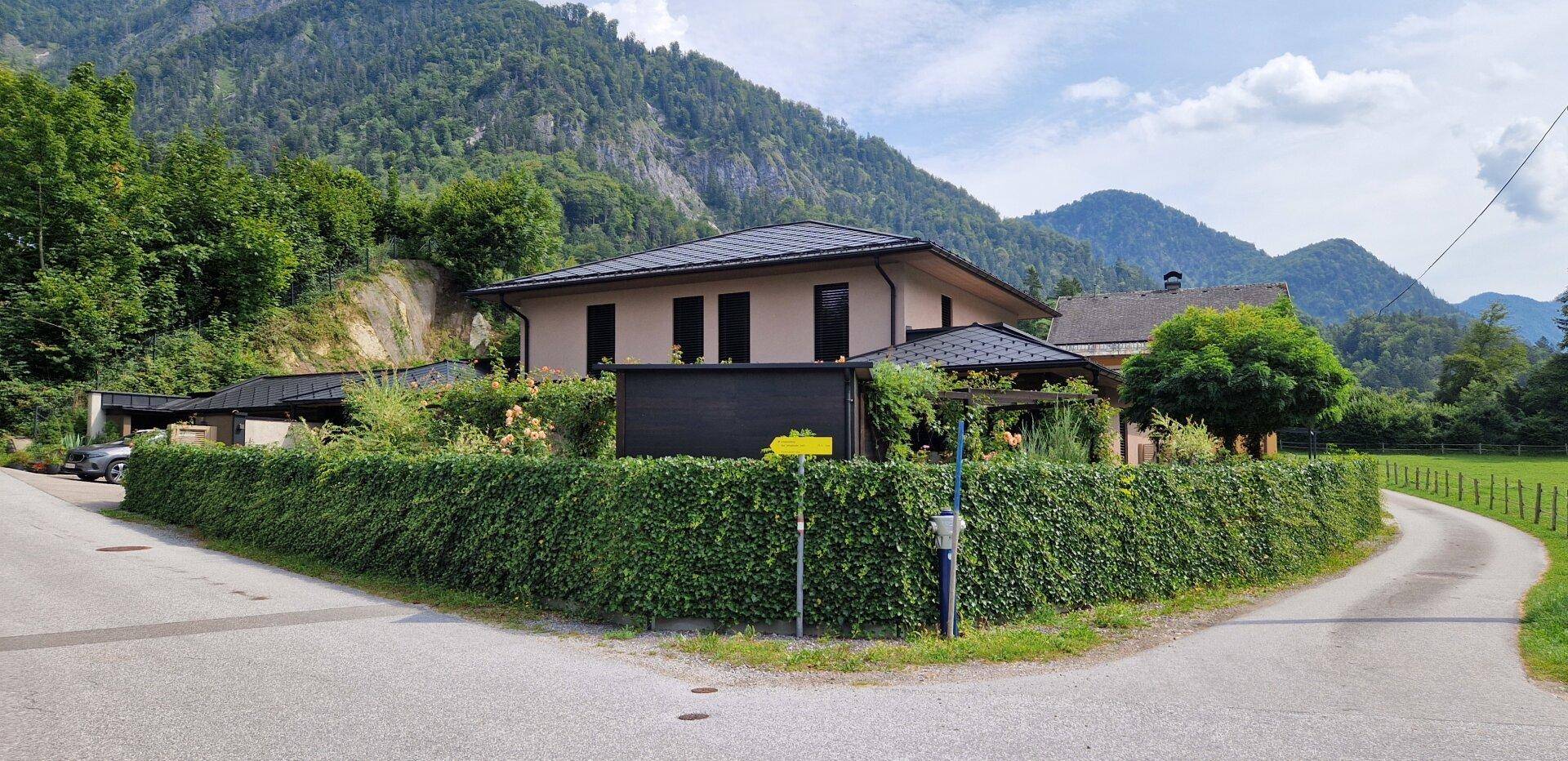 Weitläufiges Grundstück mit hoher Hecke und Blick auf die umliegende Berglandschaft.