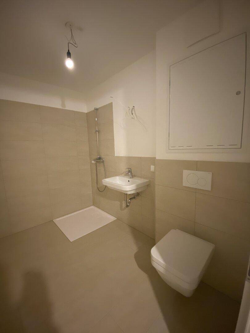 Modernes Badezimmer mit beigefarbenen Fliesen, Dusche, wandhängendem WC und Einzelwaschbecken.