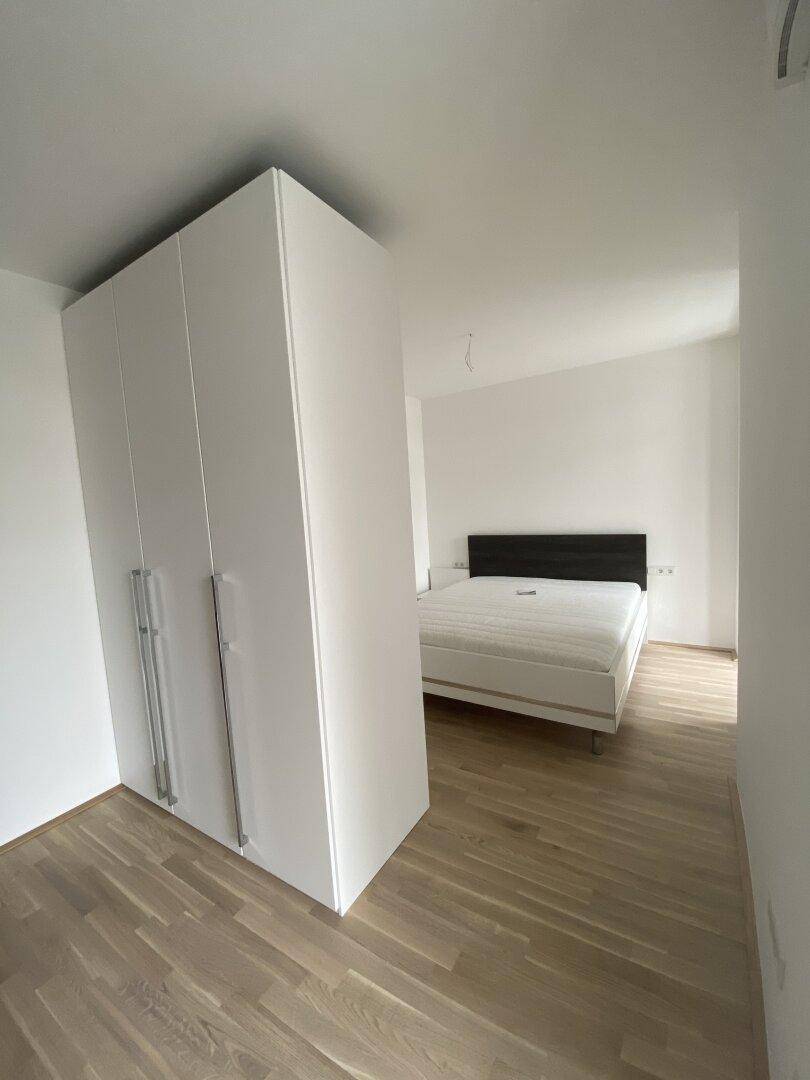 Helles Schlafzimmer mit Doppelbett, weißem Kleiderschrank und hochwertigem Holzboden.
