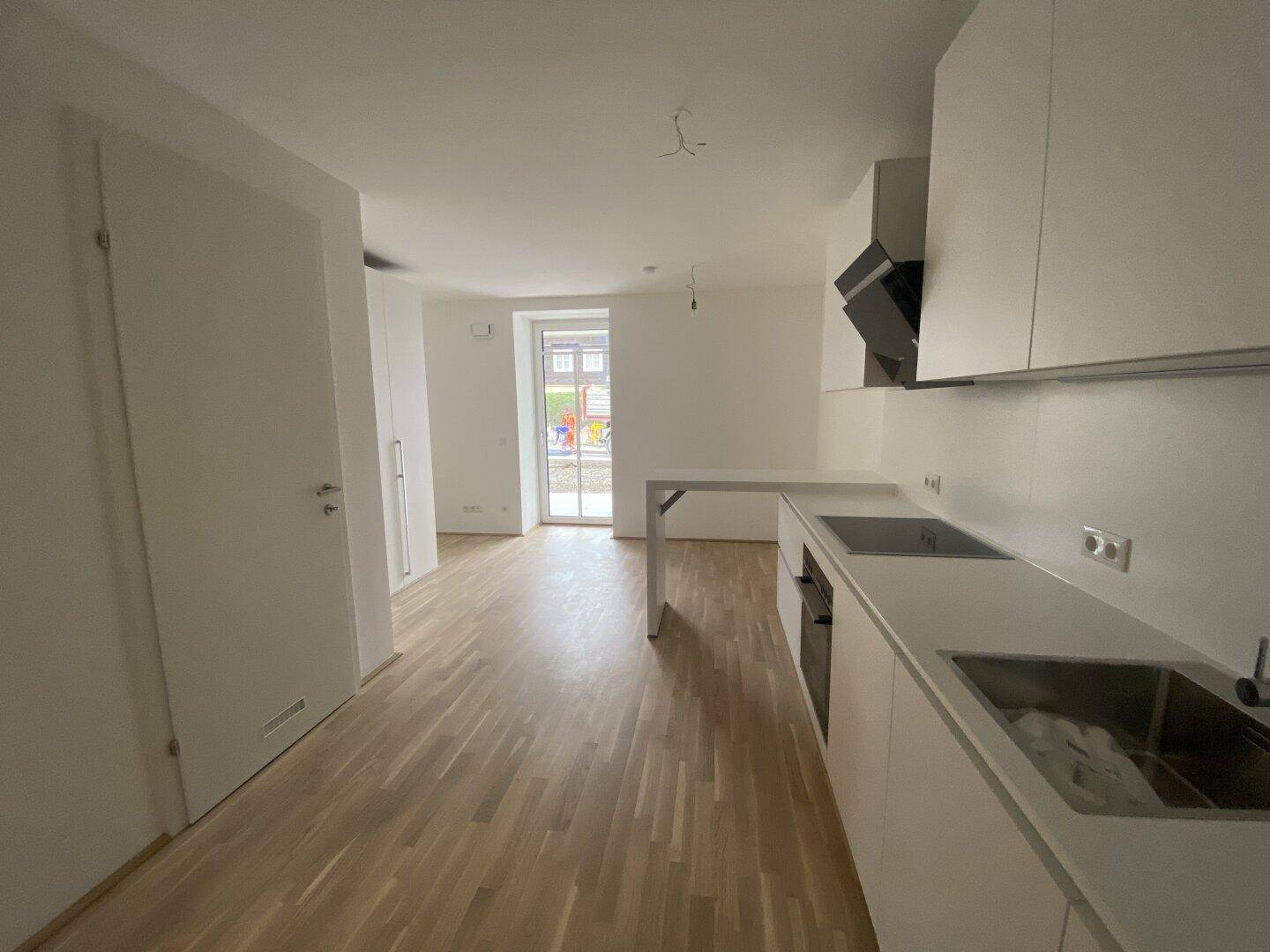 Moderne Einbauküche in Weiß mit Kochfeld, Dunstabzugshaube und Spüle, angrenzend an den Wohnbereich.