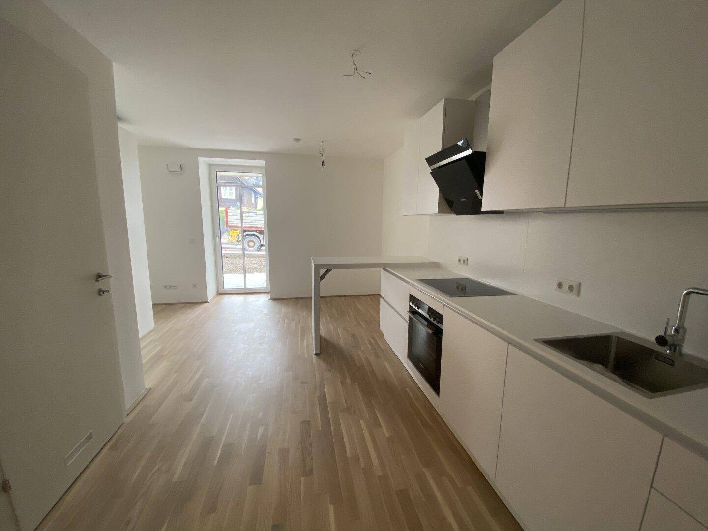 Neue weiße Einbauküche mit Kochfeld und Dunstabzugshaube in offenem Wohnbereich.