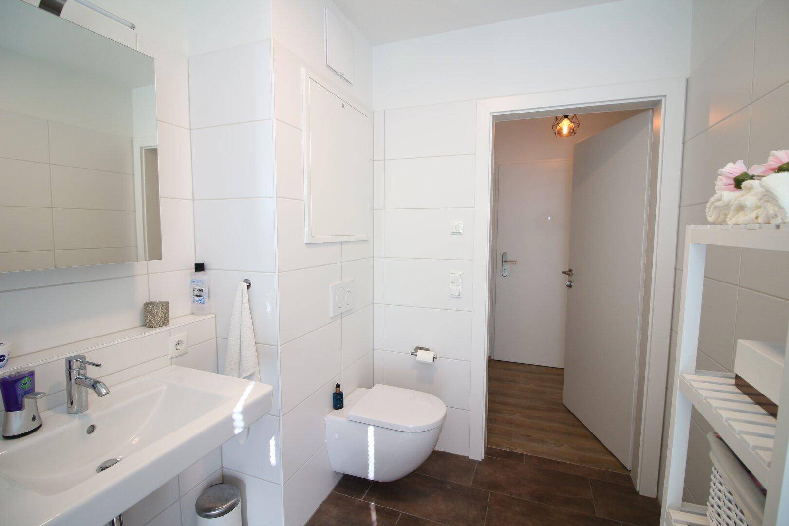 Helles Badezimmer mit weiß gefliesten Wänden, wandhängendem WC und Einzelwaschbecken.