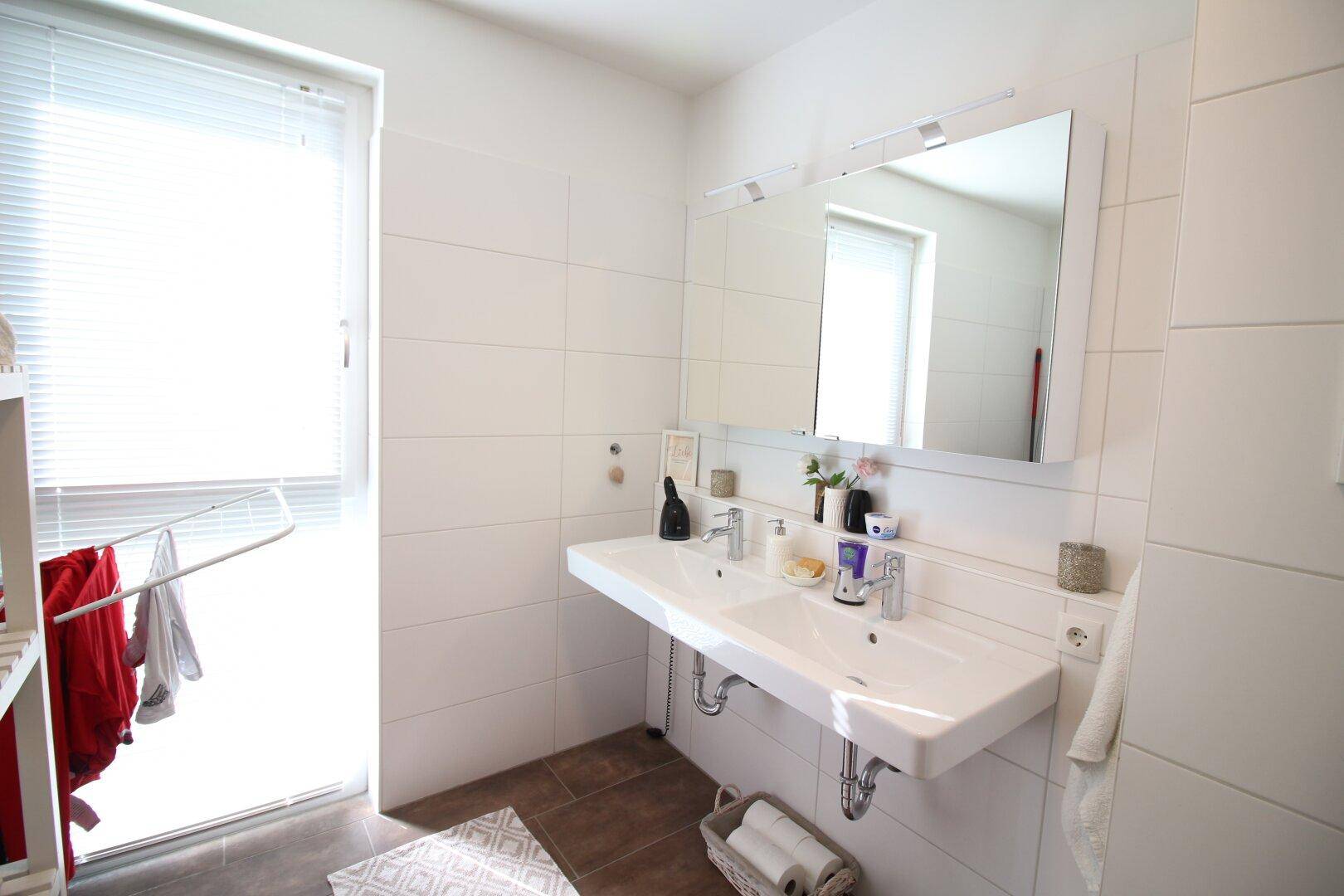 Badezimmer mit Doppelwaschbecken, großem Spiegel und Fenster für natürliches Licht.