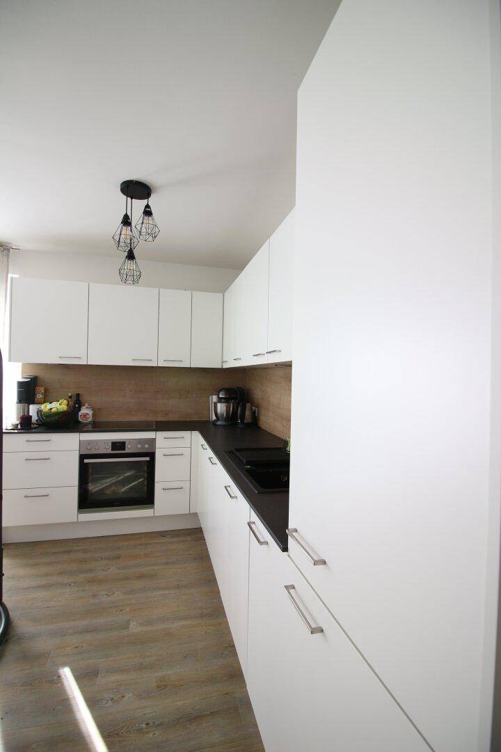 Moderne Einbauküche mit weißen Schränken, dunkler Arbeitsplatte und Holzwandverkleidung.