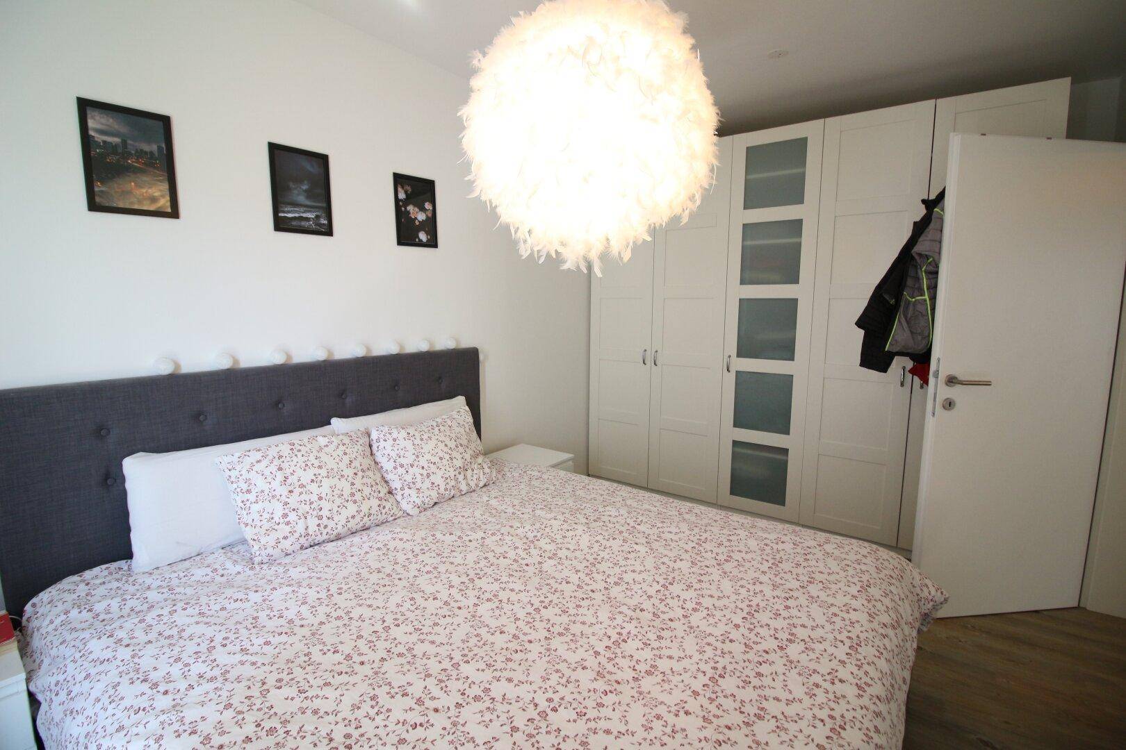 Schlafzimmer mit Doppelbett, großem weißen Kleiderschrank und dekorativer Deckenleuchte.