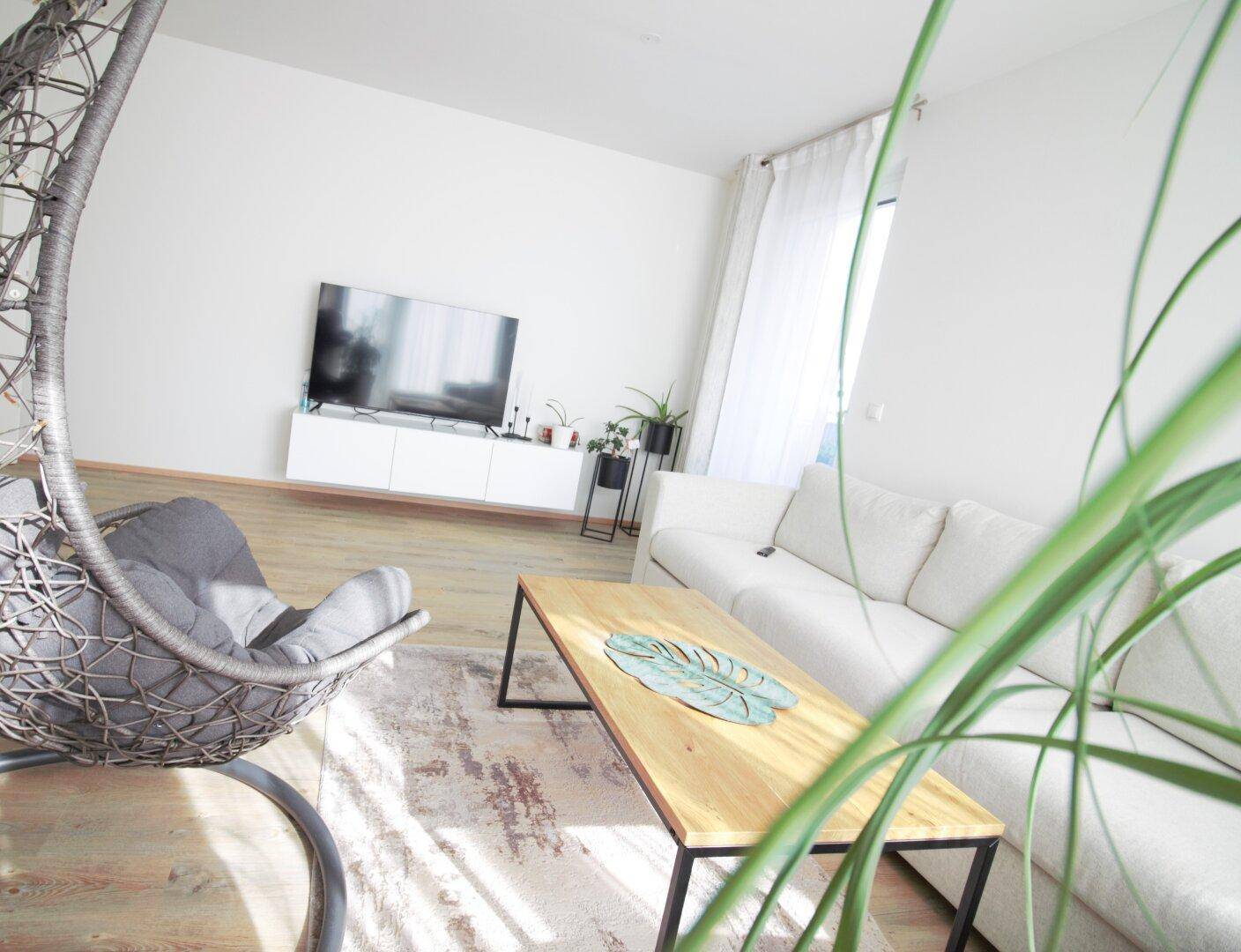 Moderner Wohnbereich mit Fernseher, Couchtisch und viel Tageslicht durch große Fenster.