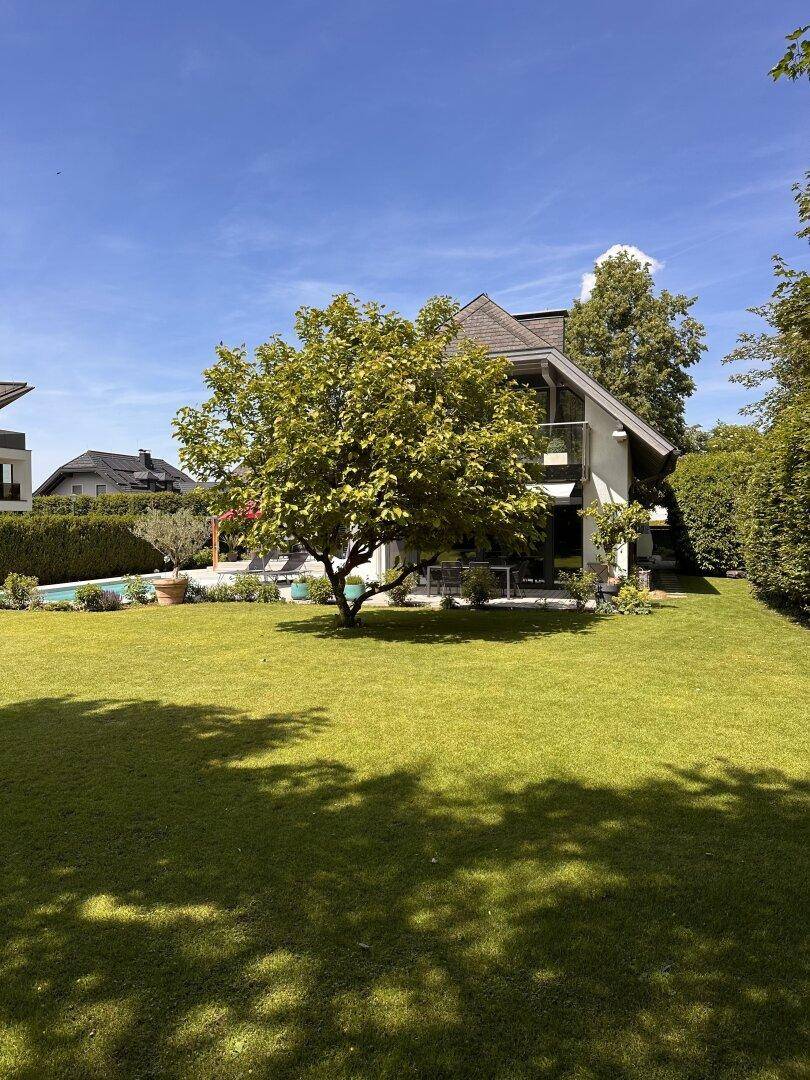 Weitläufiger, gepflegter Rasenbereich vor der modernen Villa mit Baumbestand an einem sonnigen Tag.