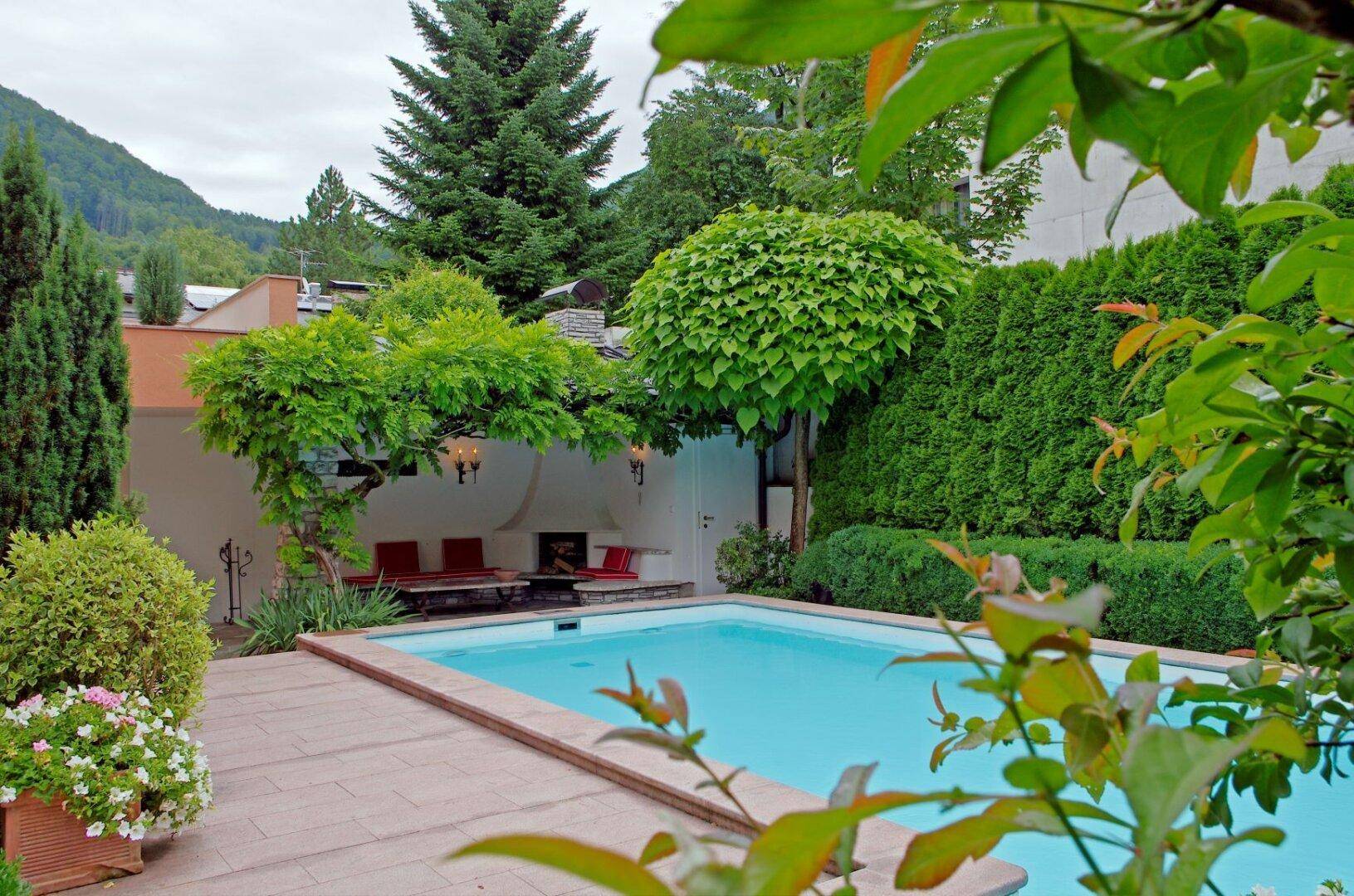 Gepflegter Gartenbereich mit Swimmingpool, gemütlichen Sitzgelegenheiten und üppiger grüner Bepflanzung.