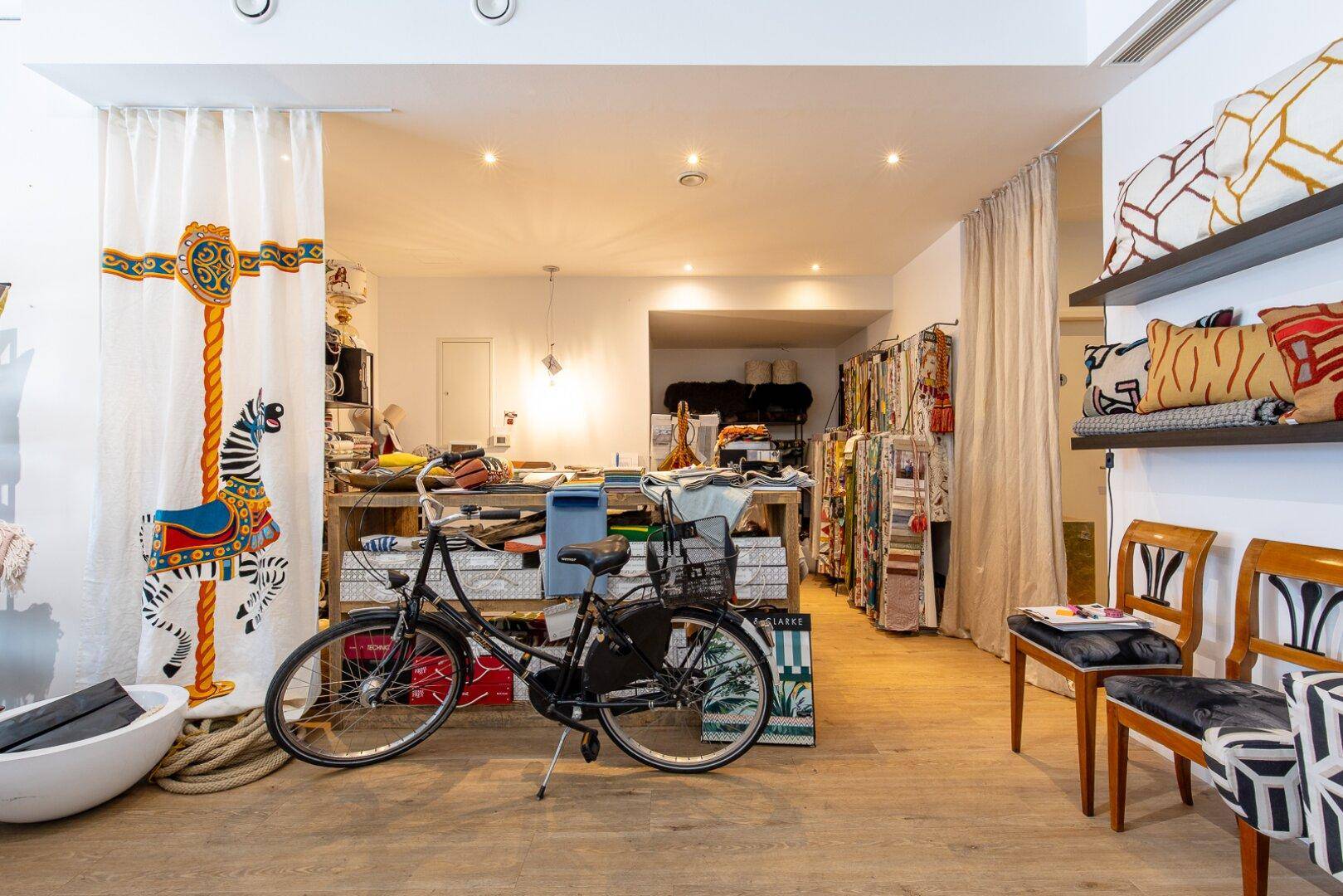 Kreativer Innenraum mit Holzboden, Stoffmustern und einem Fahrrad als Dekoration, hell beleuchtet.