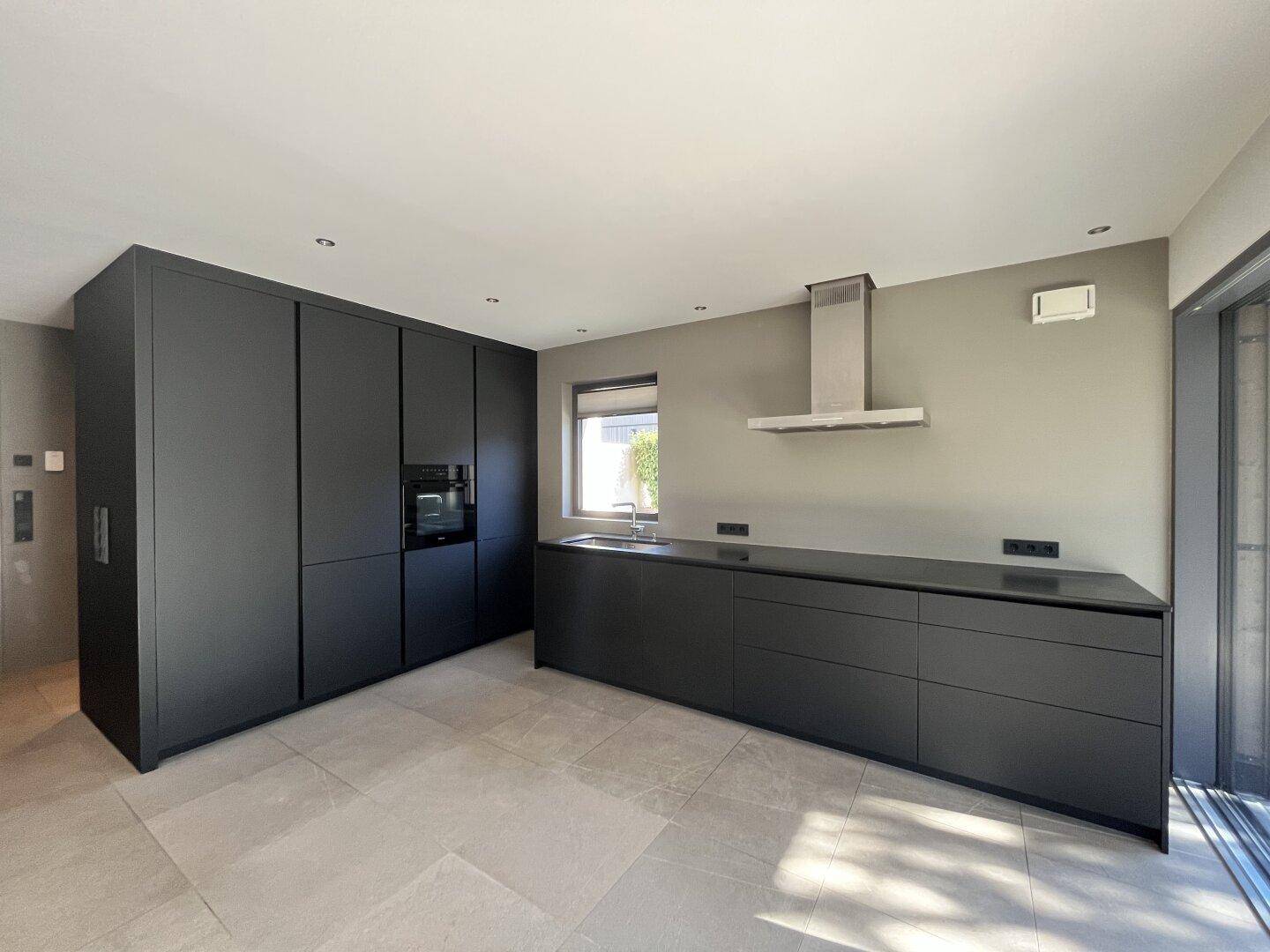 Moderne, minimalistische Küche in Schwarz mit integrierten Geräten und Fliesenboden.