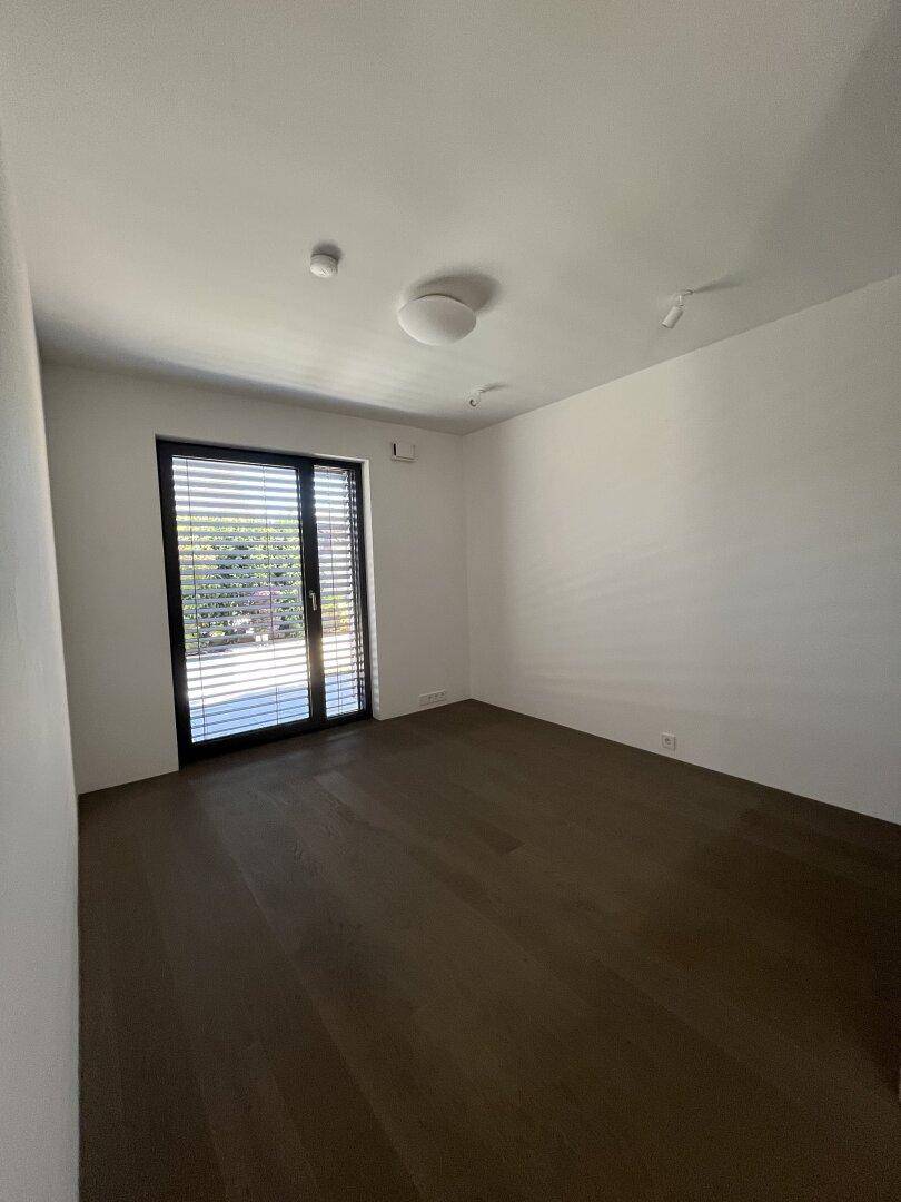 Helles, leeres Schlafzimmer mit dunklem Holzboden und Zugang zu einem Balkon oder Garten.