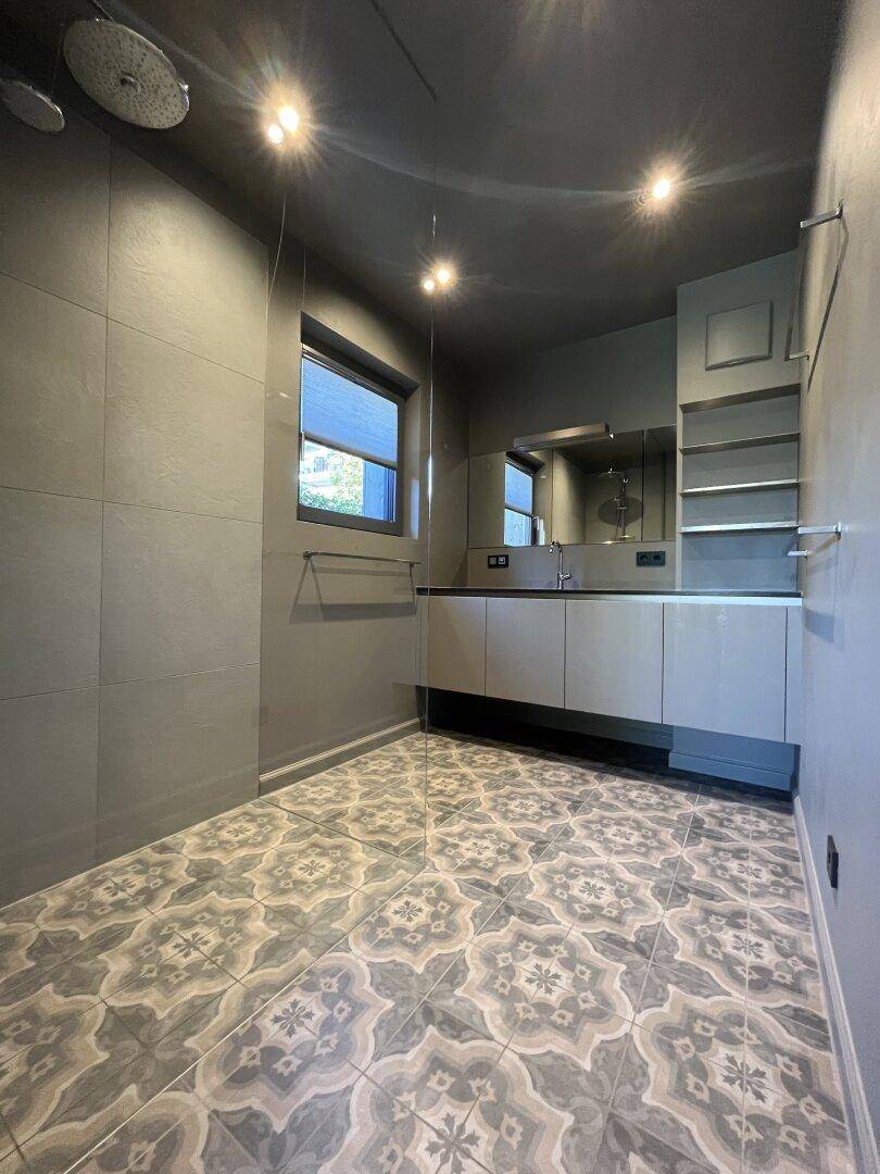 Modernes Badezimmer mit grauen Fliesen, stilvollem Waschtisch und Regendusche.