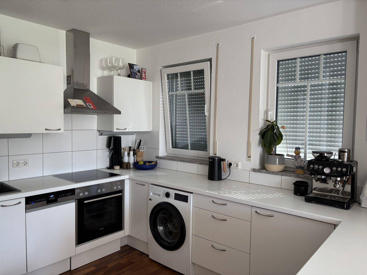 Moderne weiße Küche mit Einbaugeräten, Fliesenboden und Fenster mit Rollläden.