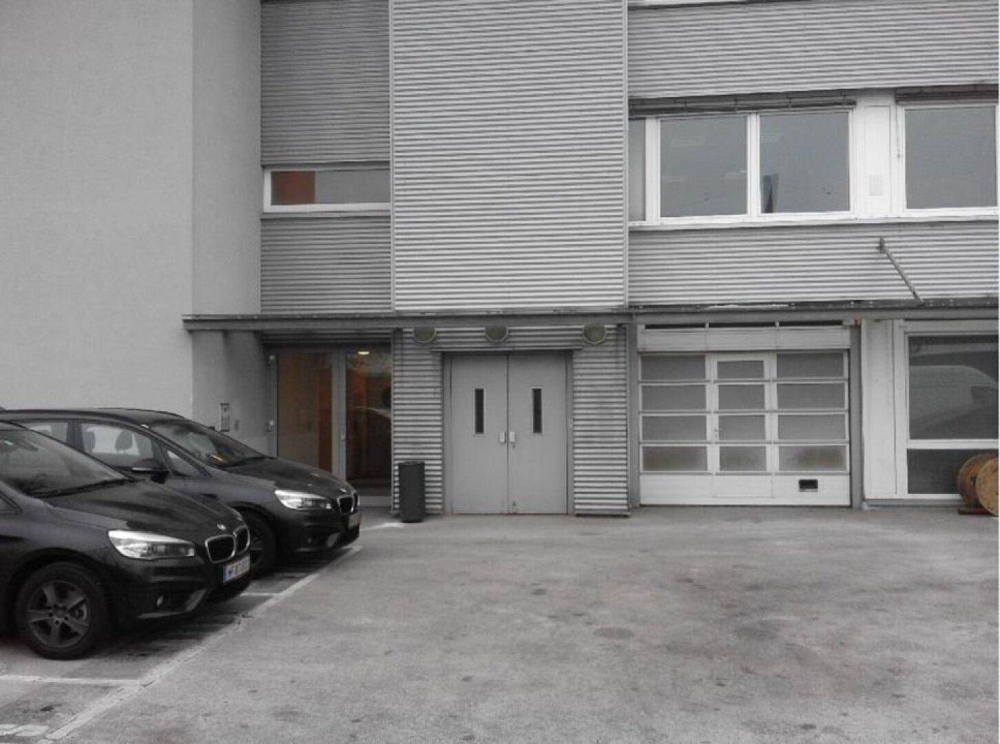 Moderne Gewerbefassade mit horizontalen Lamellen, großen Fenstern und einem Parkplatz davor.