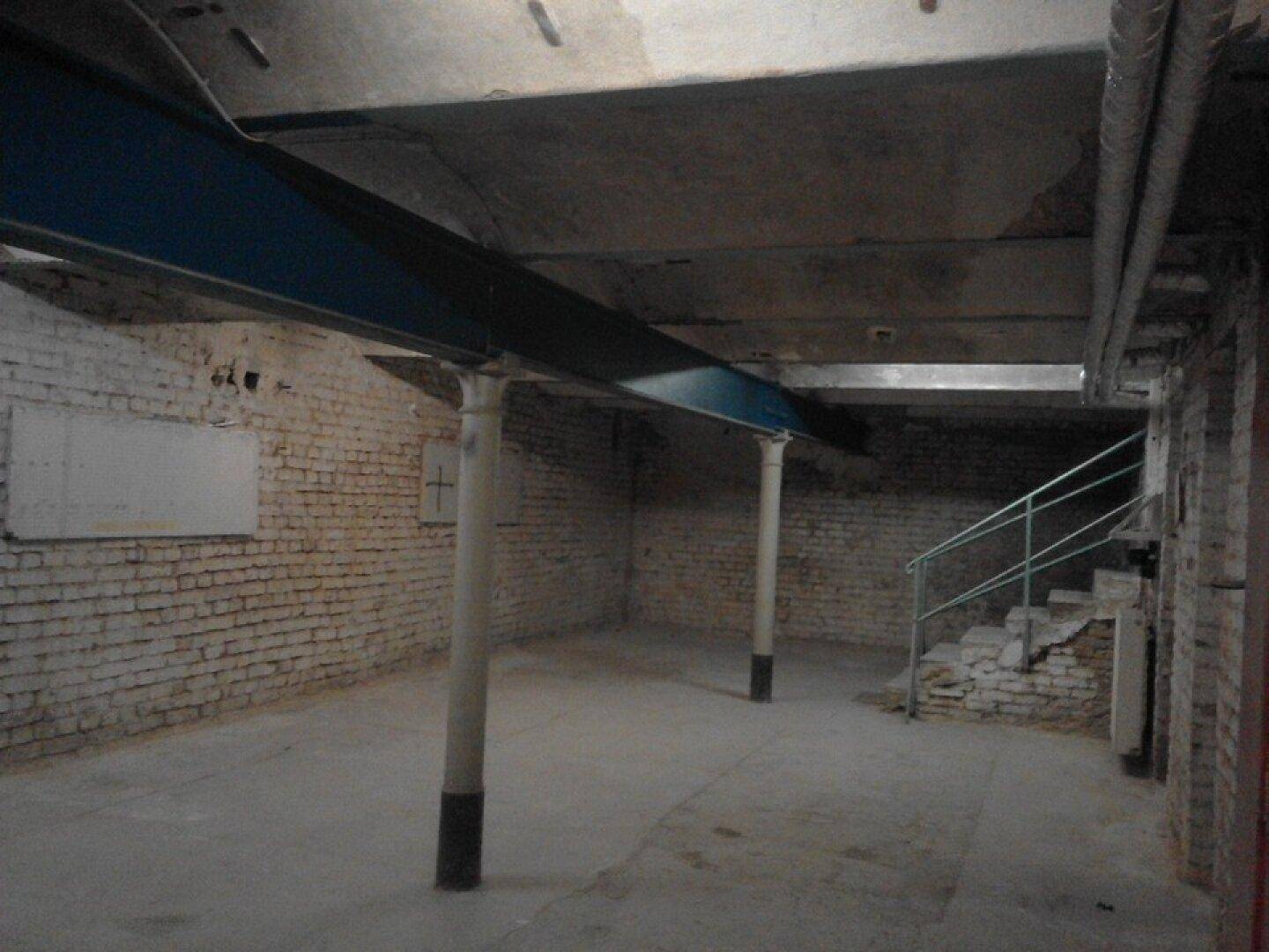Großer, leerer Kellerraum mit unverputzten Ziegelwänden, Betondecke und sichtbaren Stahlträgern.