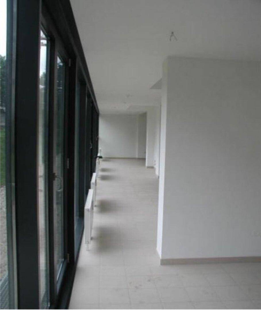 Geräumiger, unmöblierter Innenbereich mit großen Fensterfronten und einem hellen Fliesenboden.
