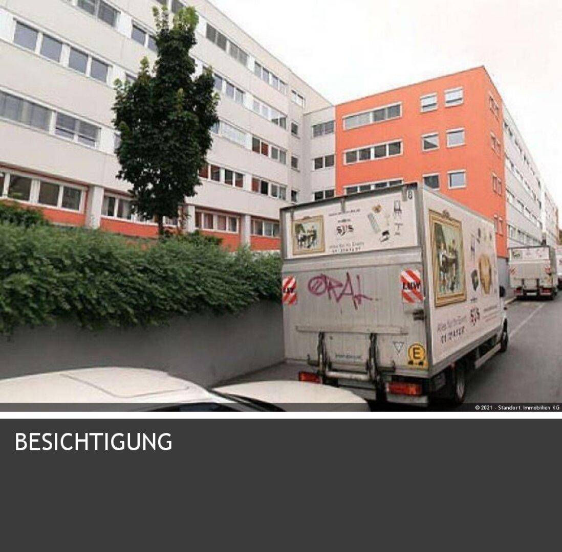 Außenansicht eines Mehrfamilienhauses mit weißer und oranger Fassade, umgeben von Grünflächen und einem Lieferwagen.