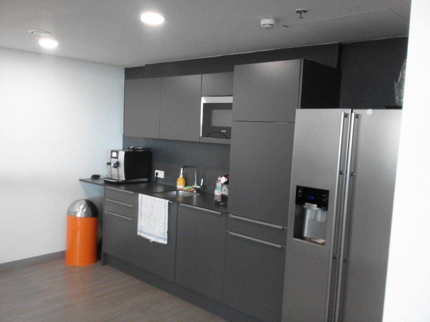 Moderne Küchenzeile mit grauen Schränken, integrierter Mikrowelle und großem Kühlschrank.