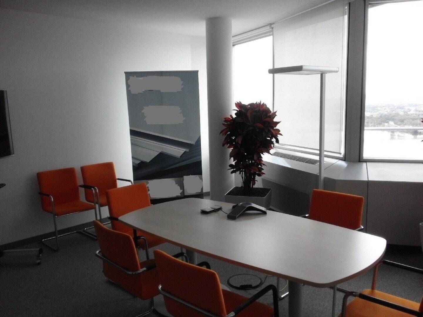 Heller Konferenzraum mit großem Tisch, orangefarbenen Stühlen und weitem Ausblick durch die Fenster.