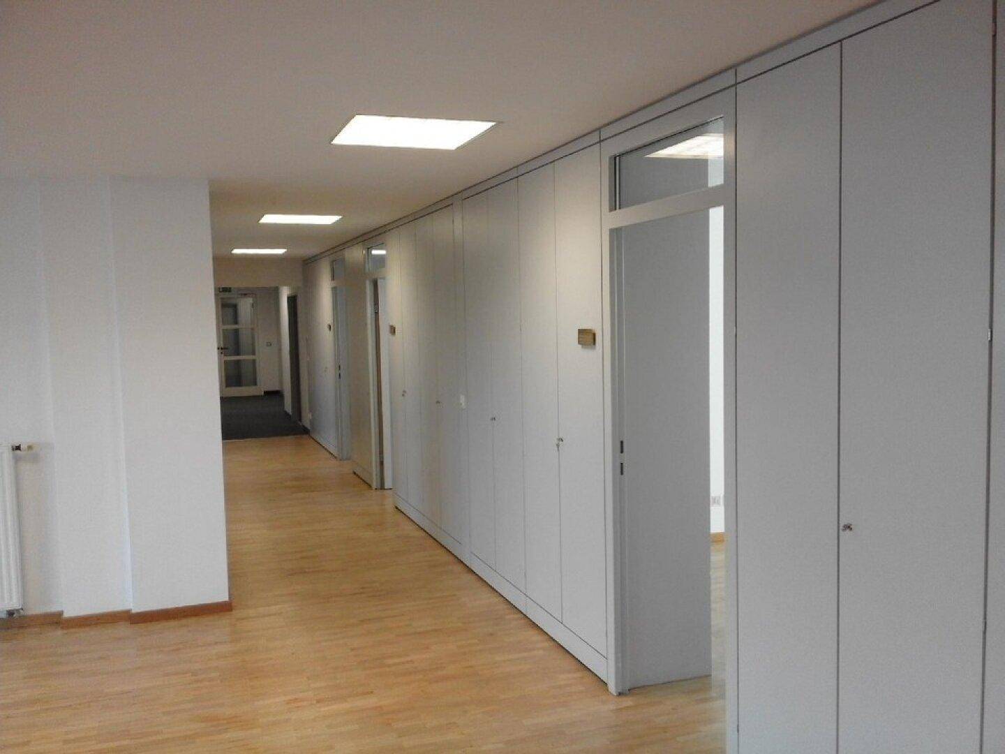 Langer Flur mit hellem Holzboden, weißen Wänden und integrierten Schränken für Stauraum.