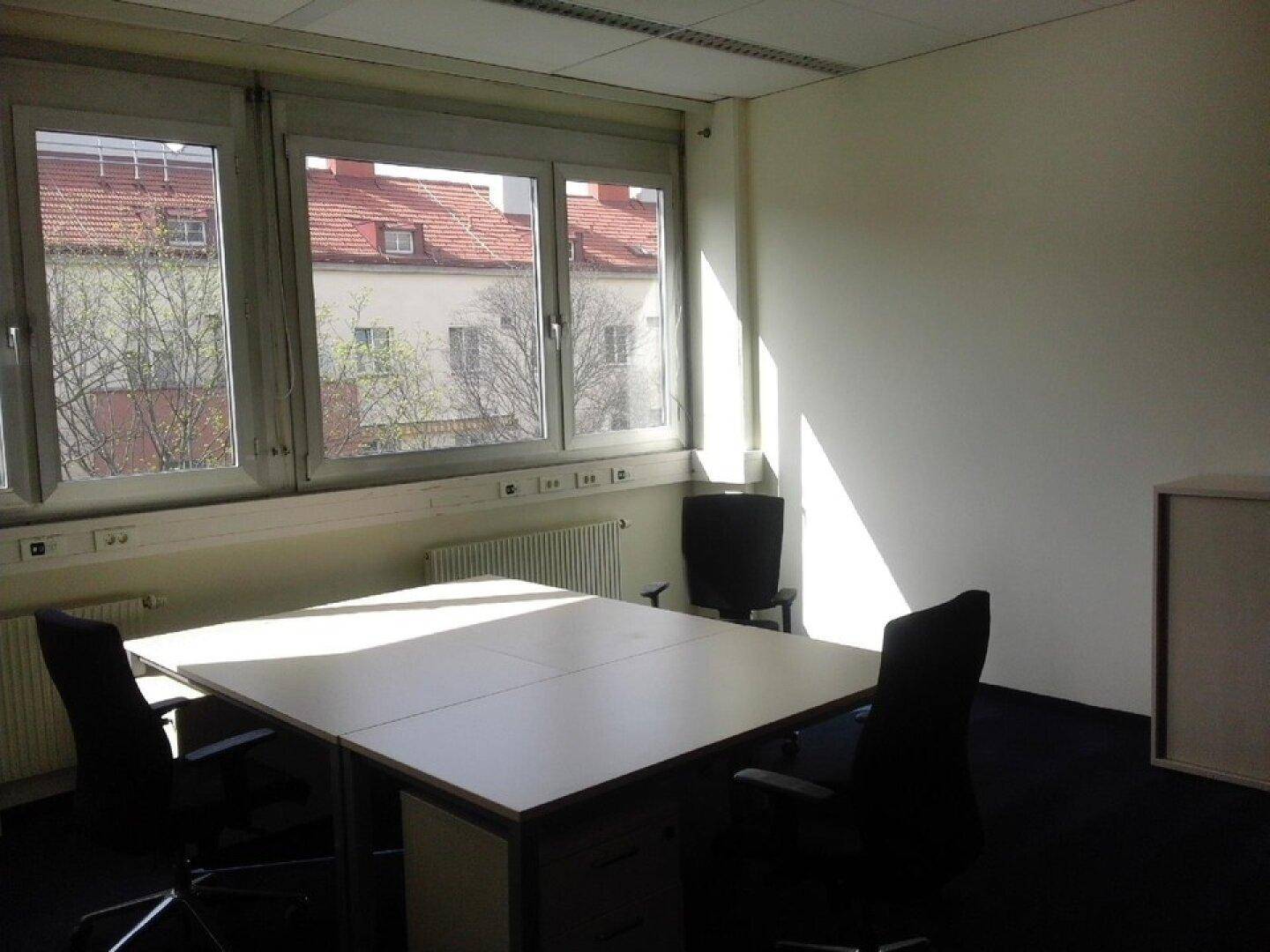Helles Büro mit großem Fenster, Teppichboden und Blick auf umliegende Gebäude, bietet eine angenehme Aussicht.