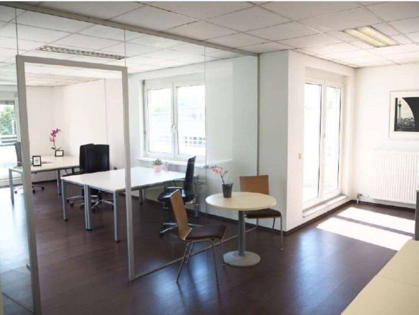 Modernes Büro mit Glaswänden, dunklem Holzboden und Zugang zu einem Balkon, ideal für kreative Teams.