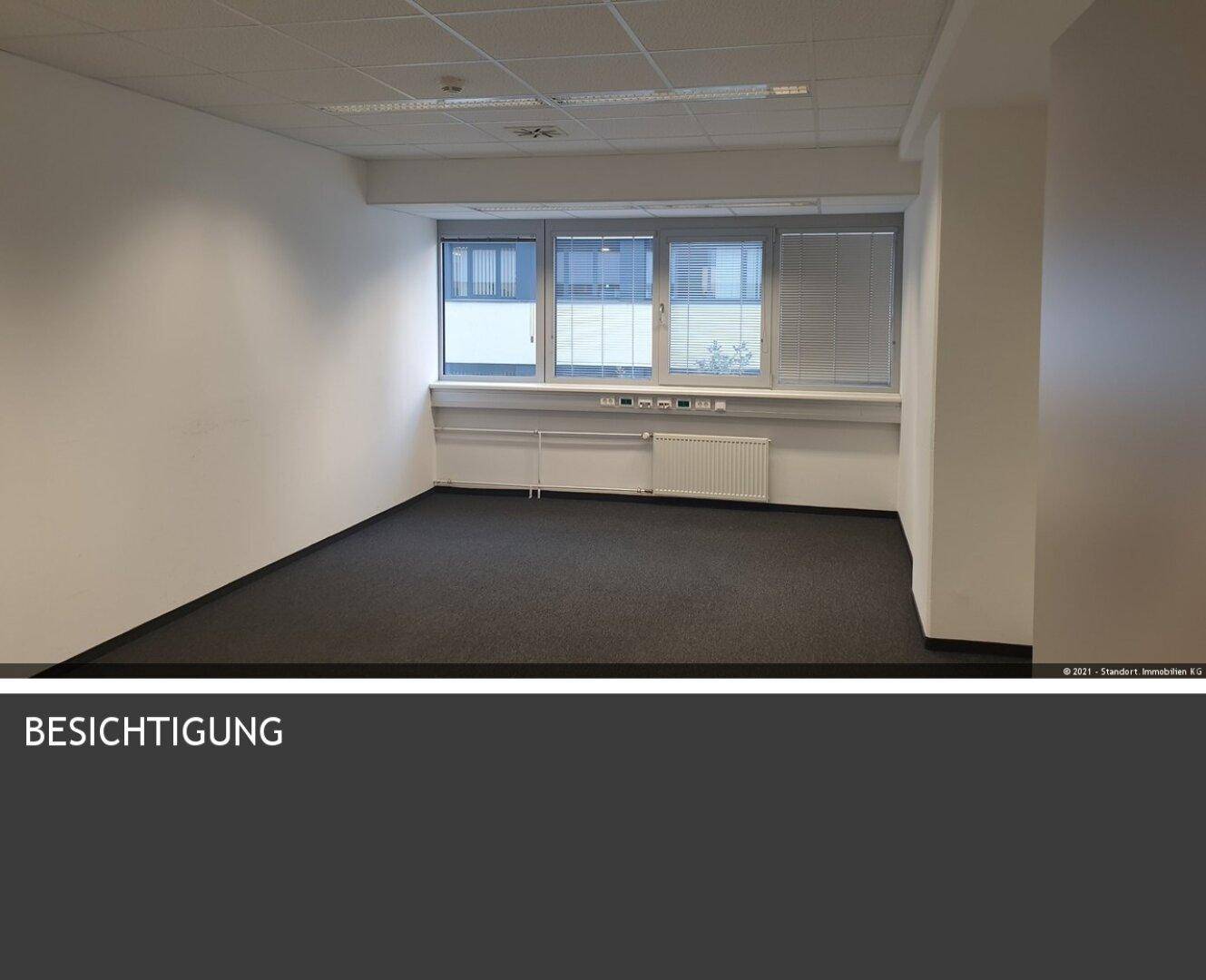 Leerer Büroraum mit Teppichboden, großen Fenstern und Blick auf die Umgebung.