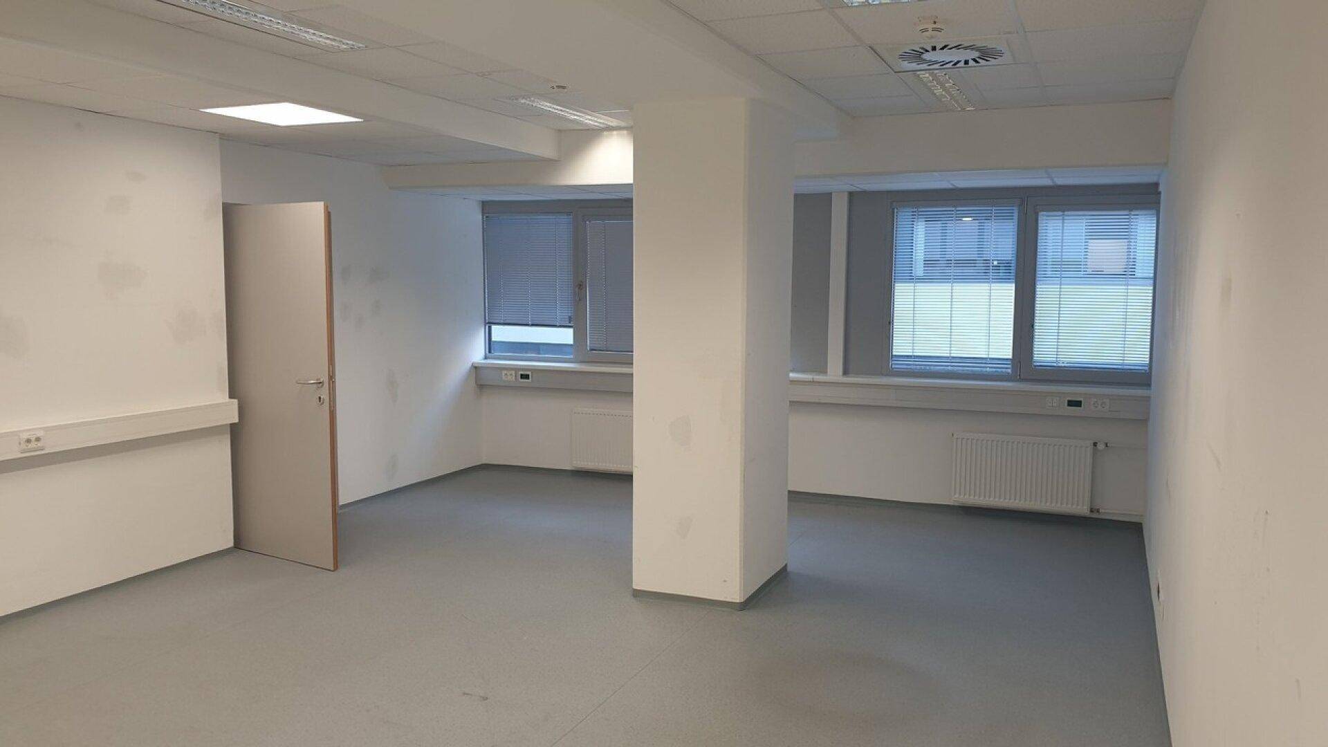 Heller Büroraum mit Säule, Fenstern und grauem Bodenbelag, bereit zur individuellen Gestaltung.