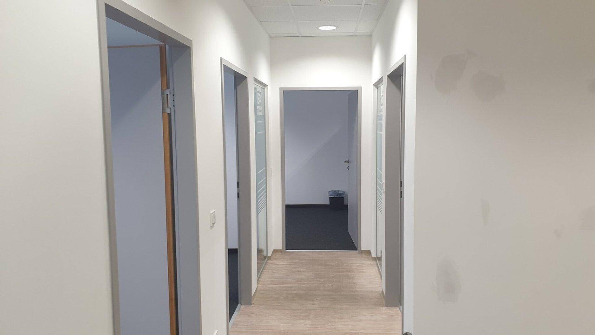 Heller Flur mit Holzboden und mehreren Türen, die zu verschiedenen Büroräumen führen.