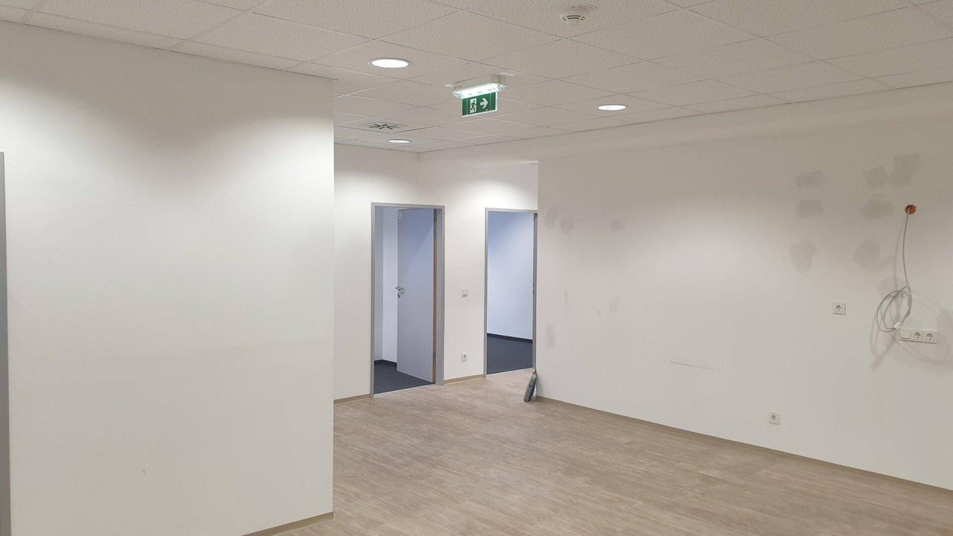 Heller, leerer Büroraum mit Holzboden und mehreren Türen, bereit zur individuellen Gestaltung.