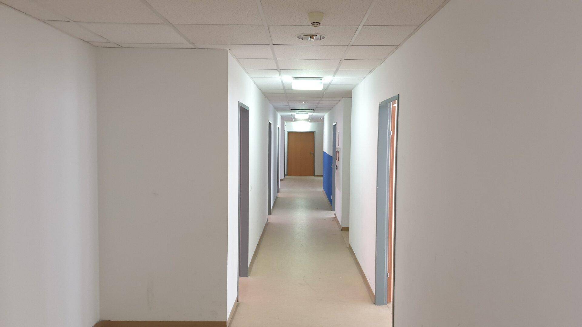 Langer, leerer Flur mit mehreren Türen, abgehängter Decke und heller Beleuchtung.