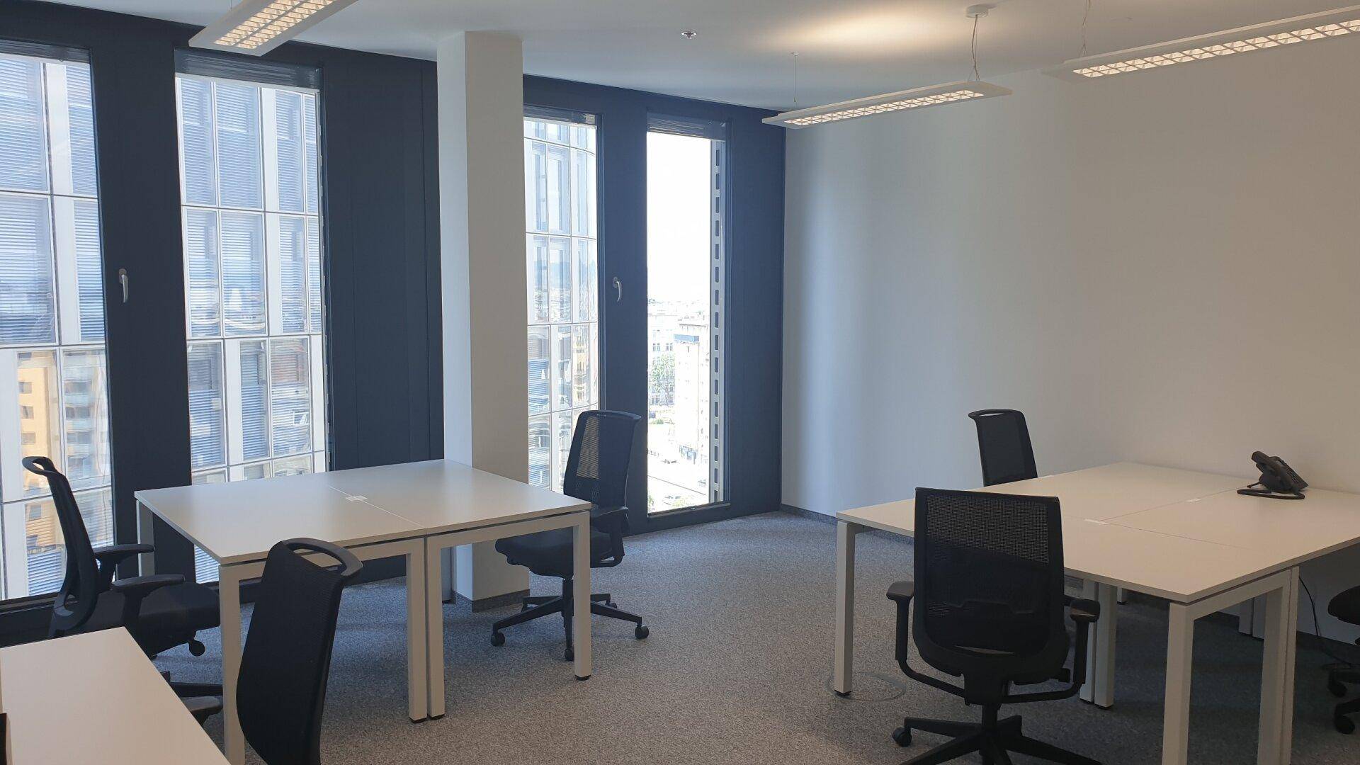 Offener Bürobereich mit mehreren leeren Schreibtischen und raumhohen Fenstern für viel Licht.