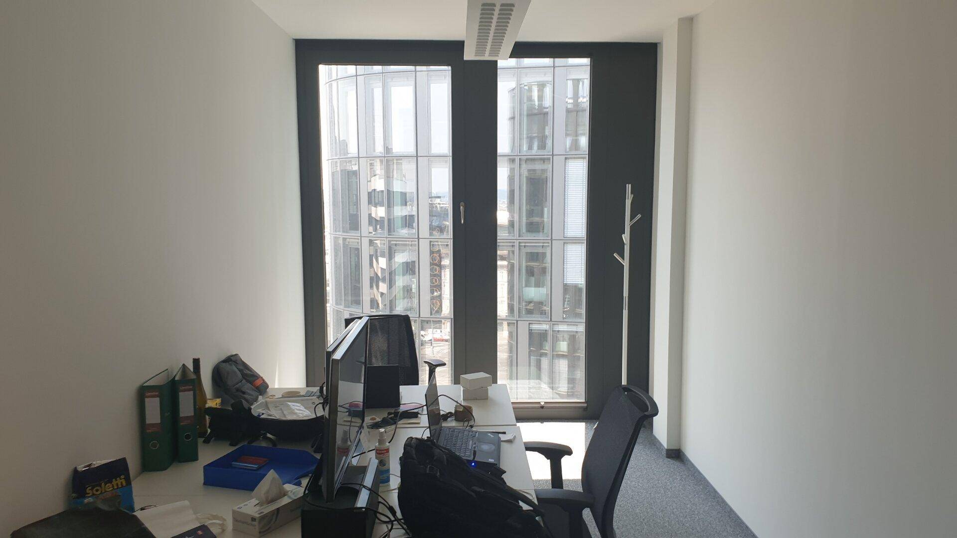 Einzelner Arbeitsplatz in einem hellen Büro mit Blick auf die umliegenden Gebäude durch große Fenster.