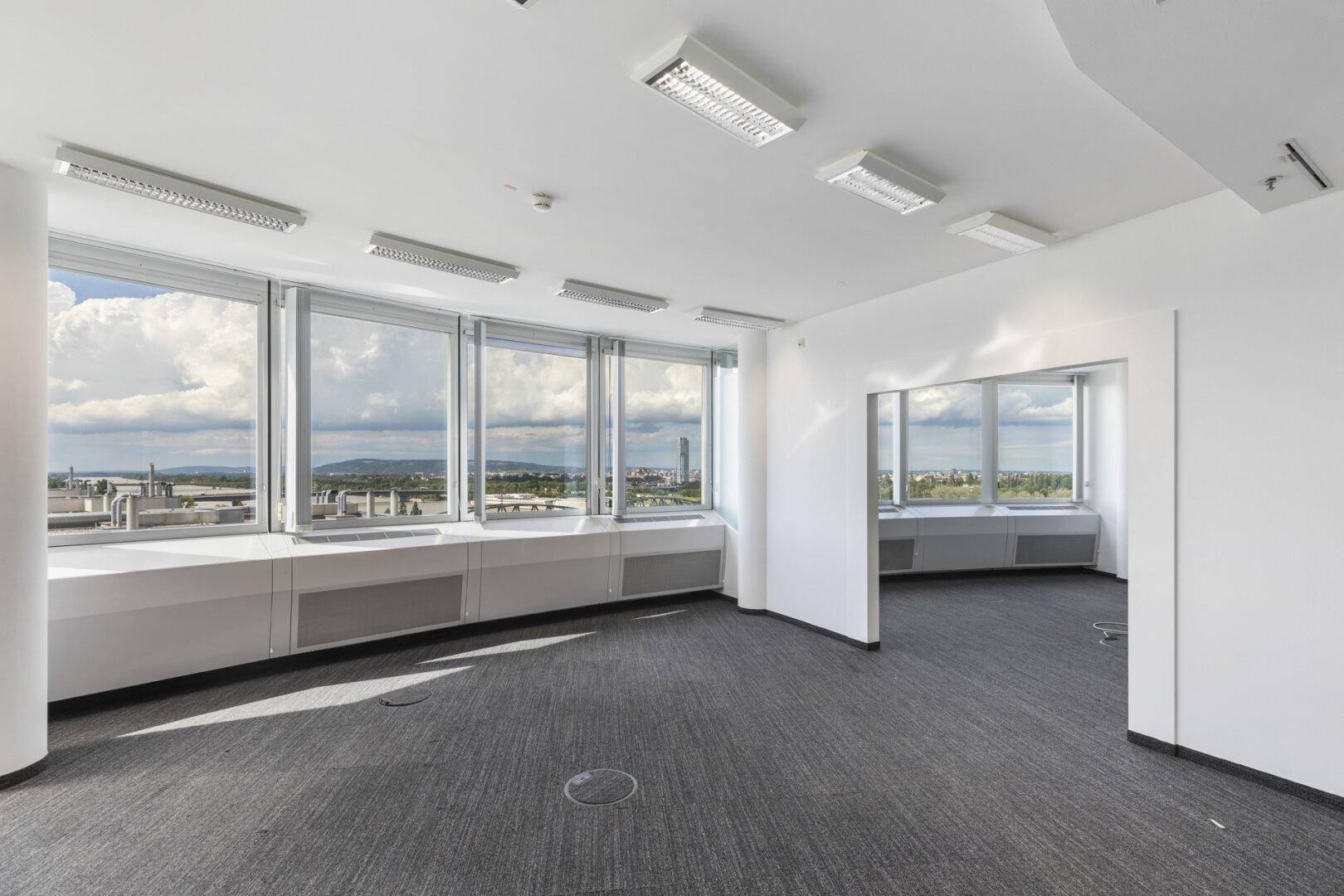 Helles Büro mit großen Fenstern, Teppichboden und weitem Blick über die Umgebung.