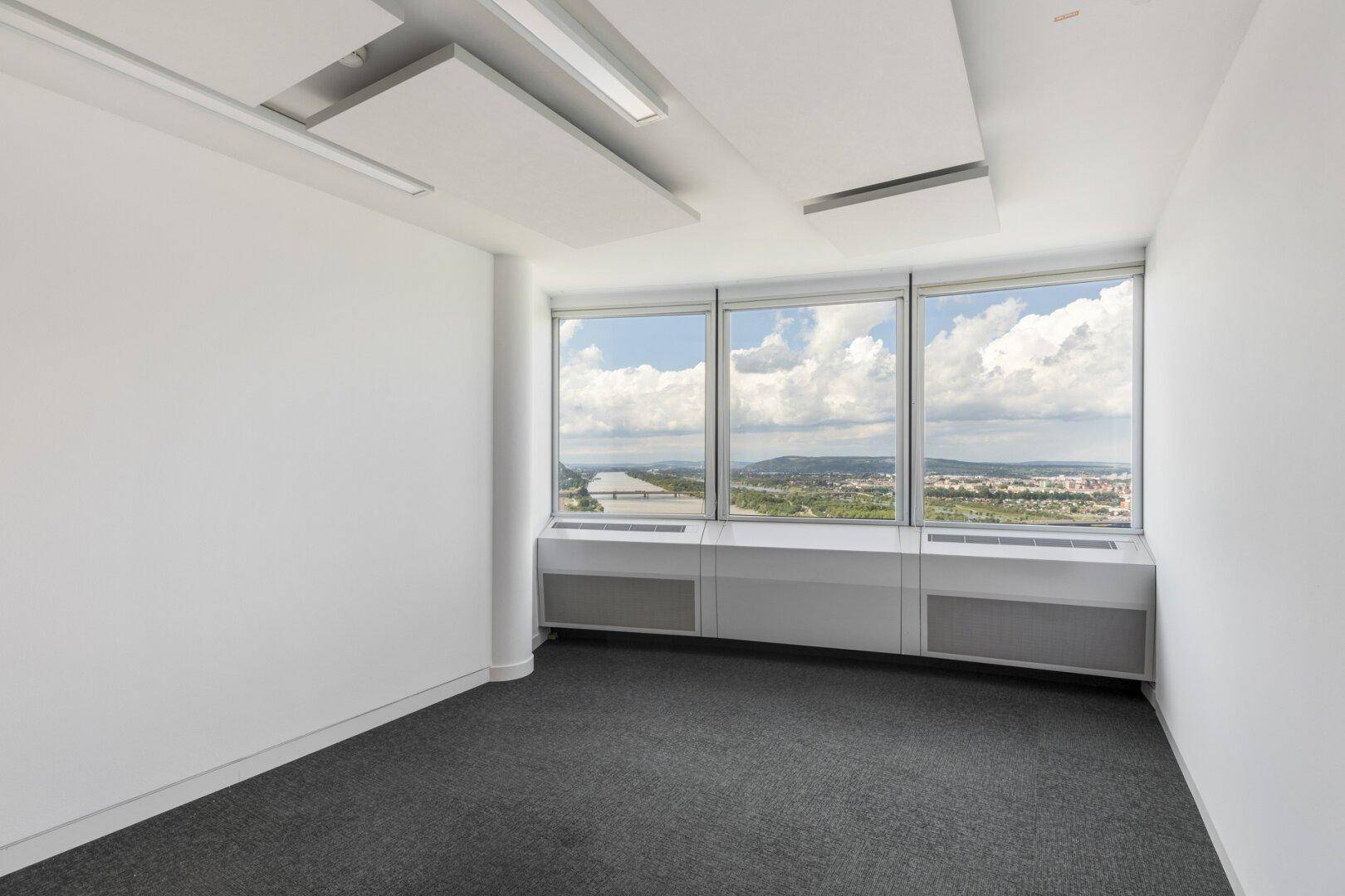 Heller Büroraum mit großen Fenstern, Teppichboden und weitem Blick über Stadt und Fluss.