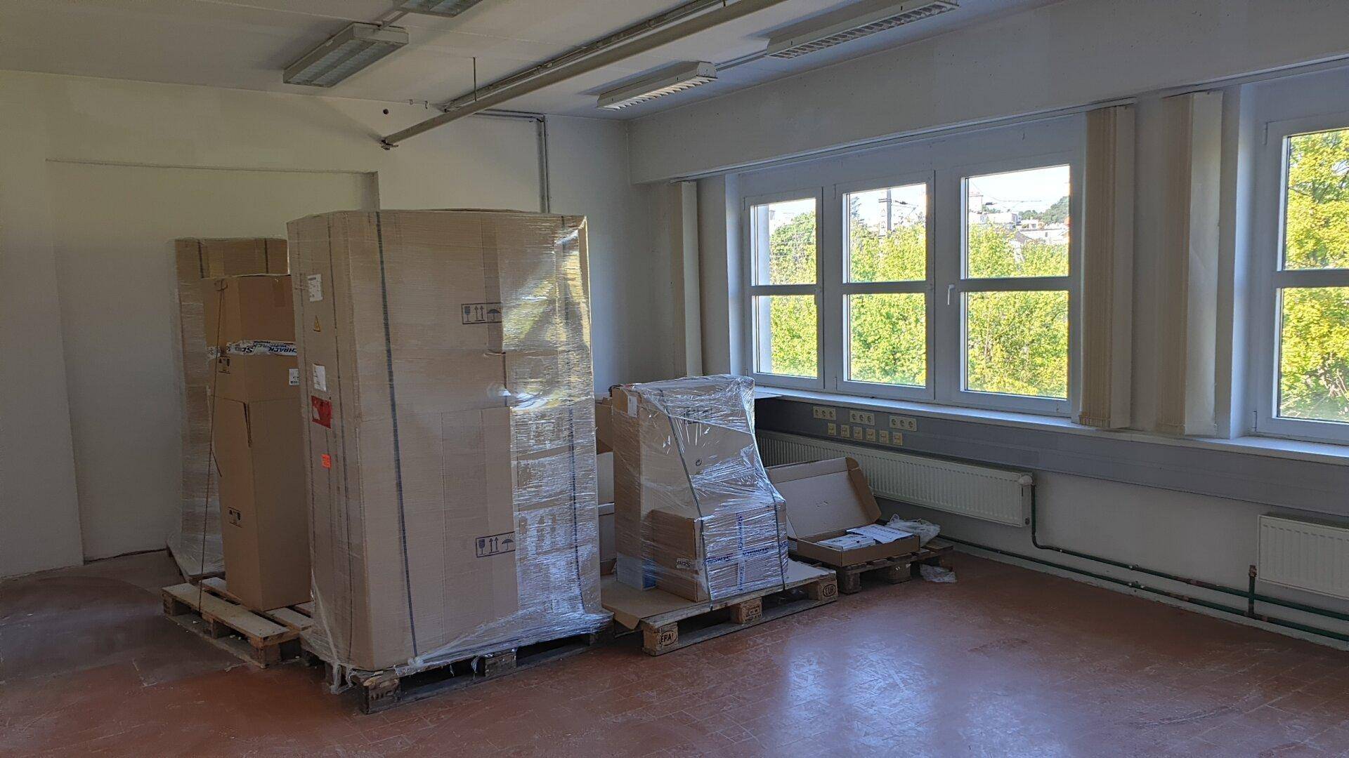 Lagerraum mit verpackten Gütern auf Paletten und großen Fenstern, die einen Blick ins Grüne bieten.