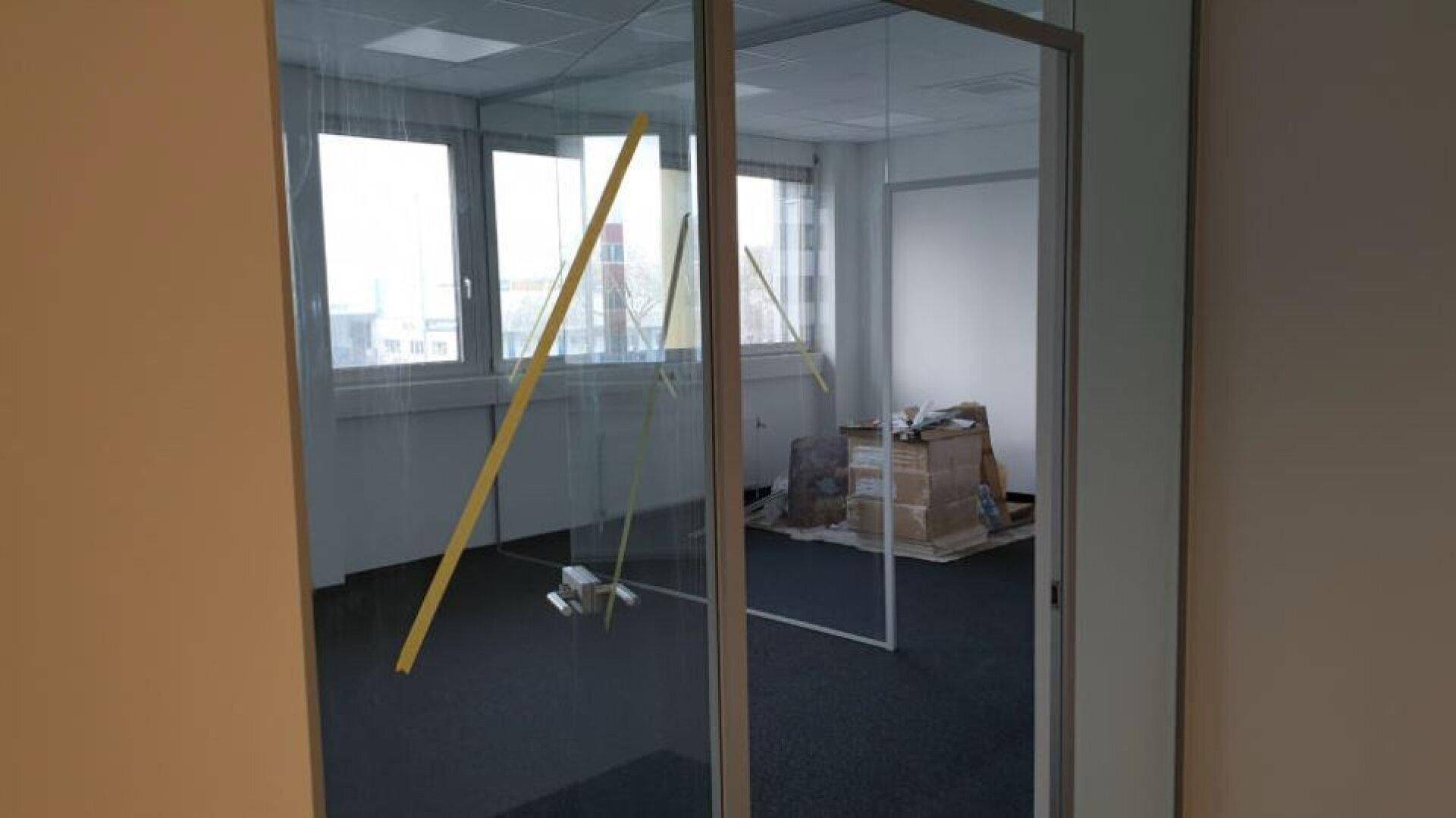 Bürofläche mit Glaswänden und Teppichboden, bereit für die Einrichtung, mit Blick nach draußen.
