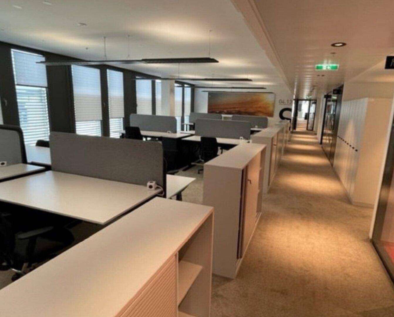 Langer Bürogang mit offenen Arbeitsbereichen, integrierten Schränken und Teppichboden.