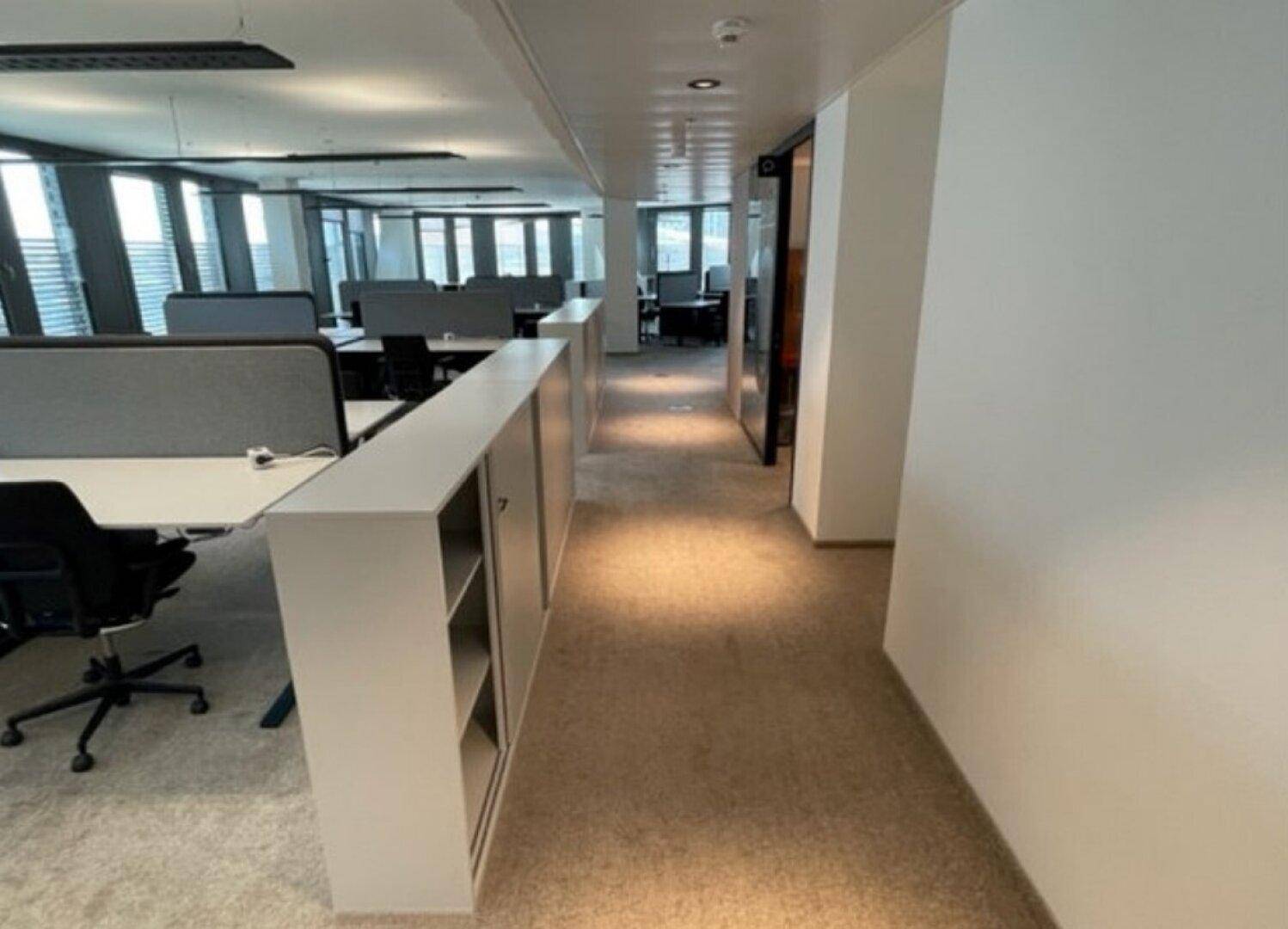 Heller, moderner Großraumbüro mit Teppichboden, Schreibtischen und Stauraum entlang des Ganges.